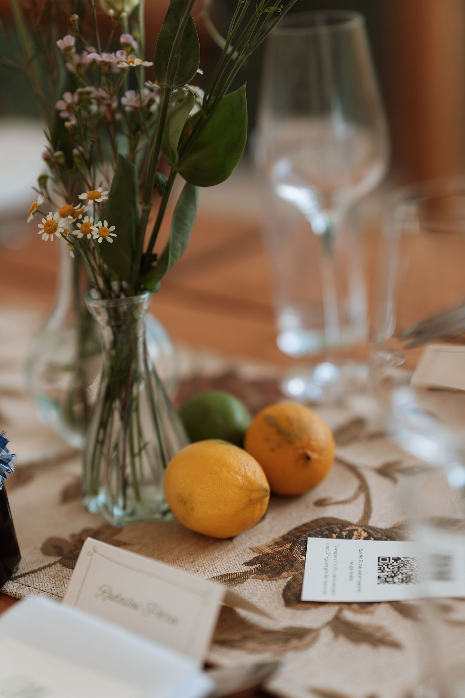 Table setting with lemons, wine glasses, and delicate floral centerpiece in a rustic wedding reception.