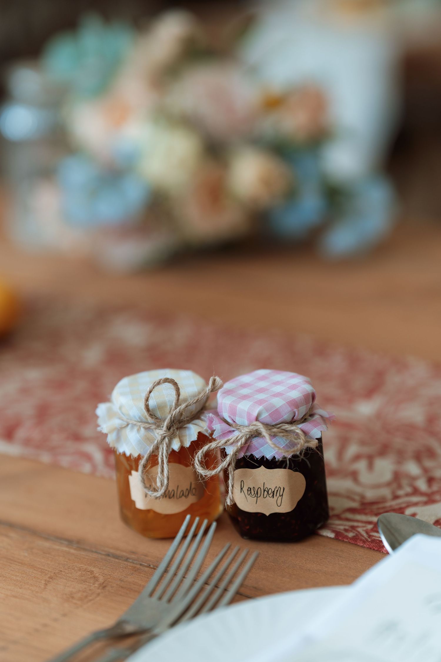 Two small decorative jam jars with fabric tops and twine on wooden surface.