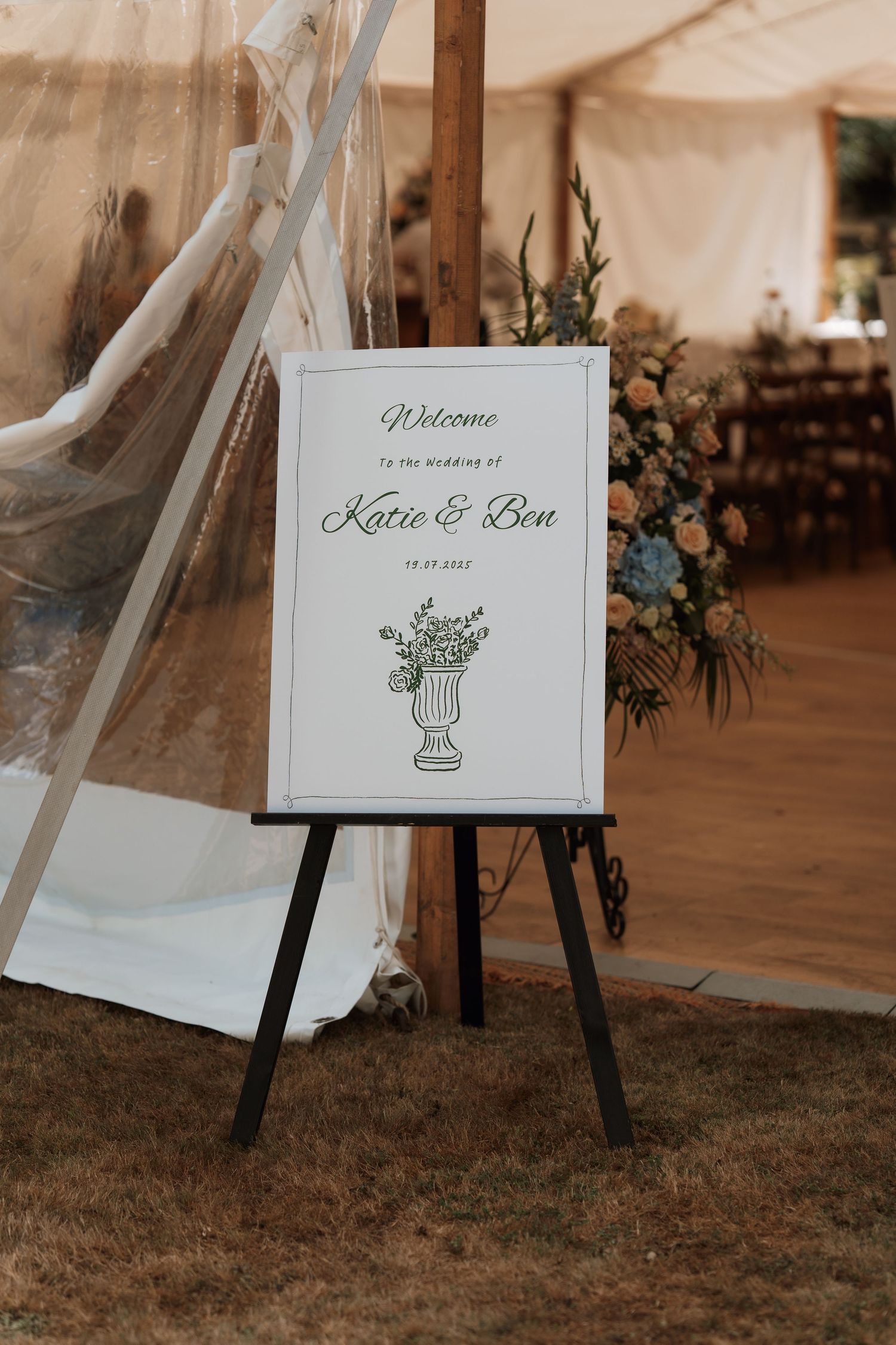 A wedding welcome sign with cactus illustration displayed on an easel near a white tent.
