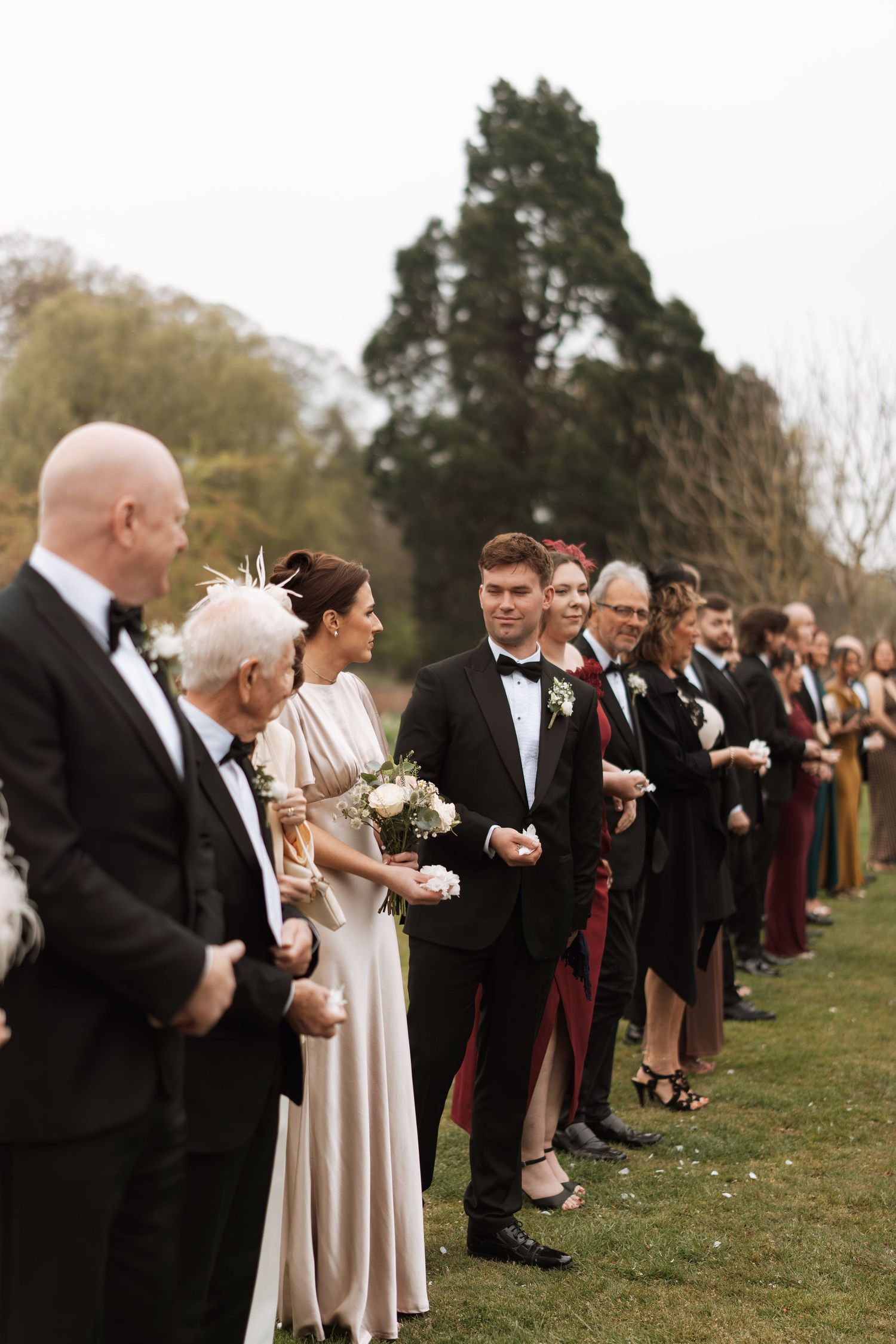 Wedding guests lined up outdoors in formal attire during a ceremony.