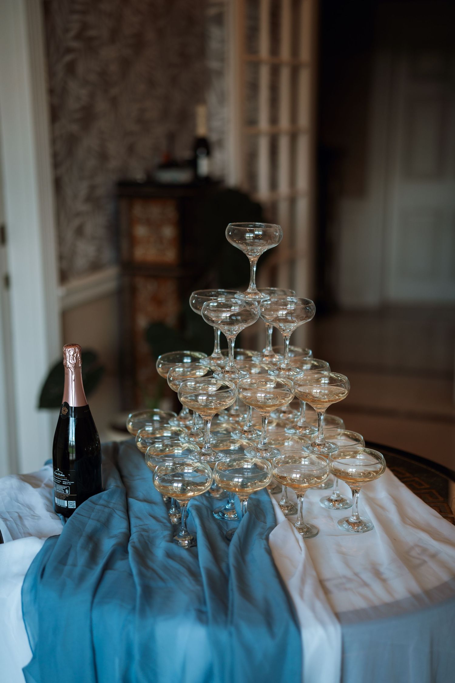 Champagne tower setup with glasses arranged pyramid-style on blue and white linens.