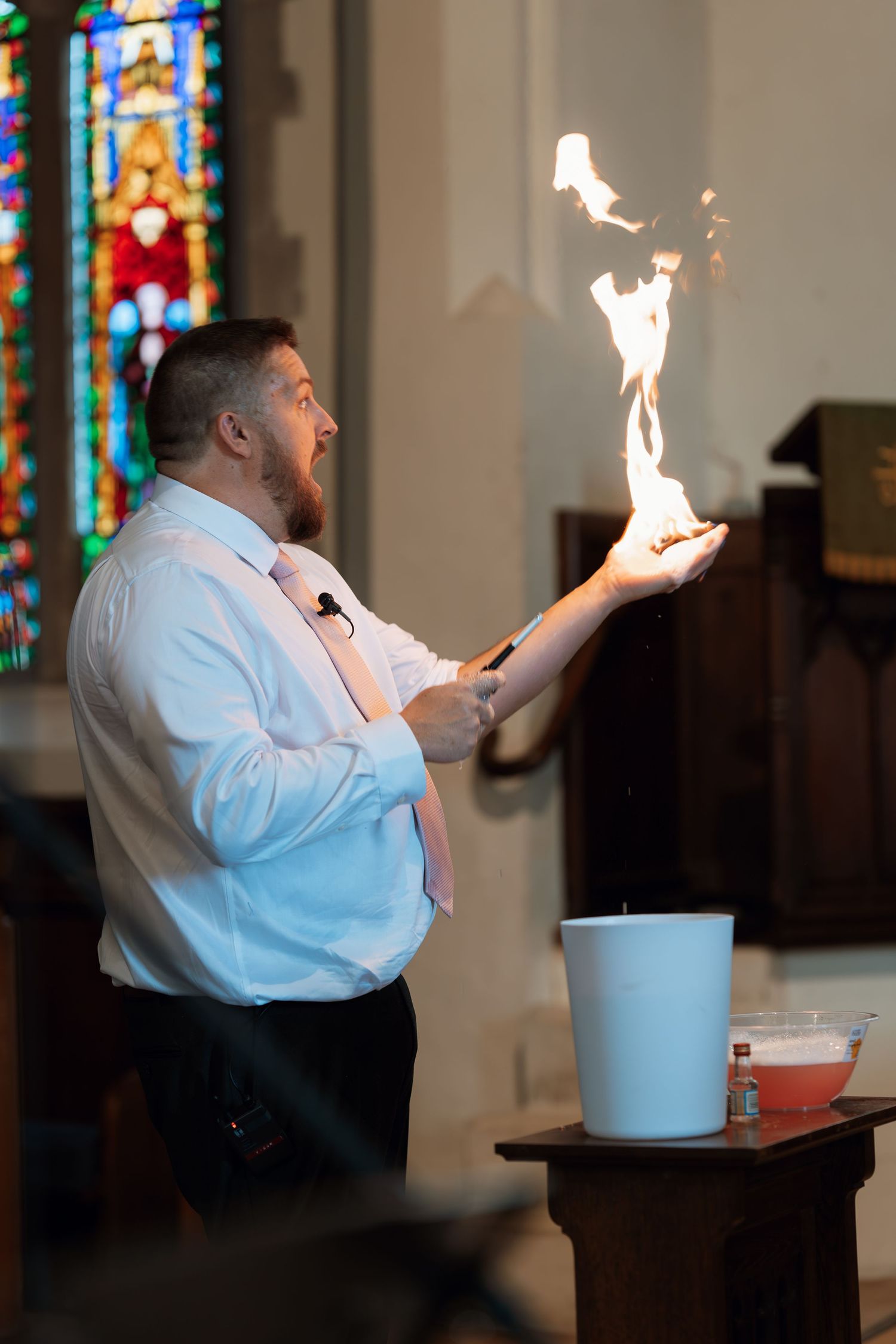 A performer in white clothing demonstrating fire tricks inside a church with stained glass windows.