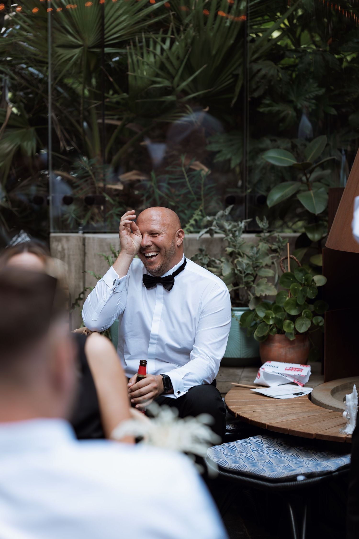 Wedding reception scene with guests in formal attire seated in lush garden setting.