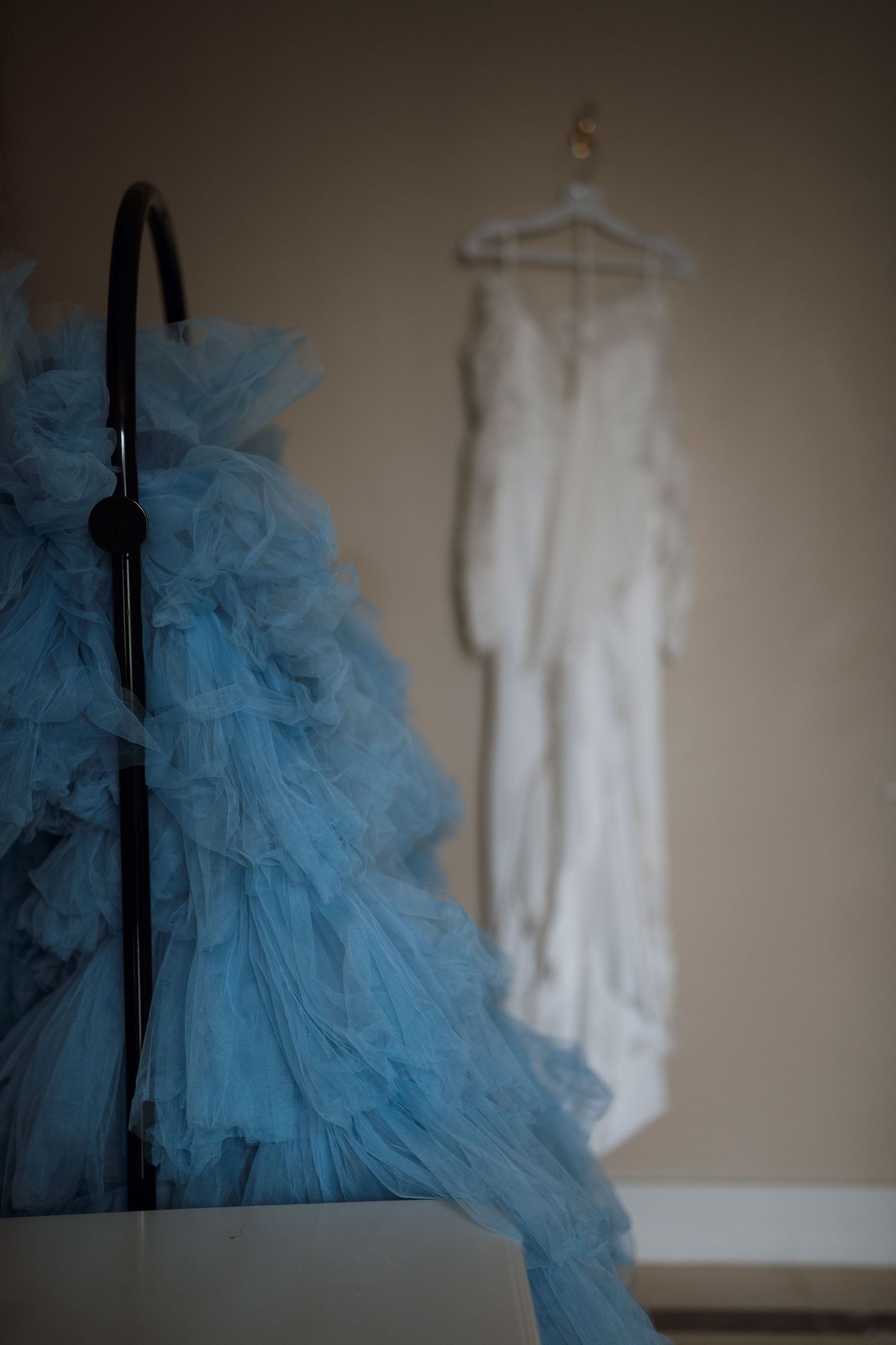 A blue tulle dress and white wedding gown hanging side by side in preparation for a special event.