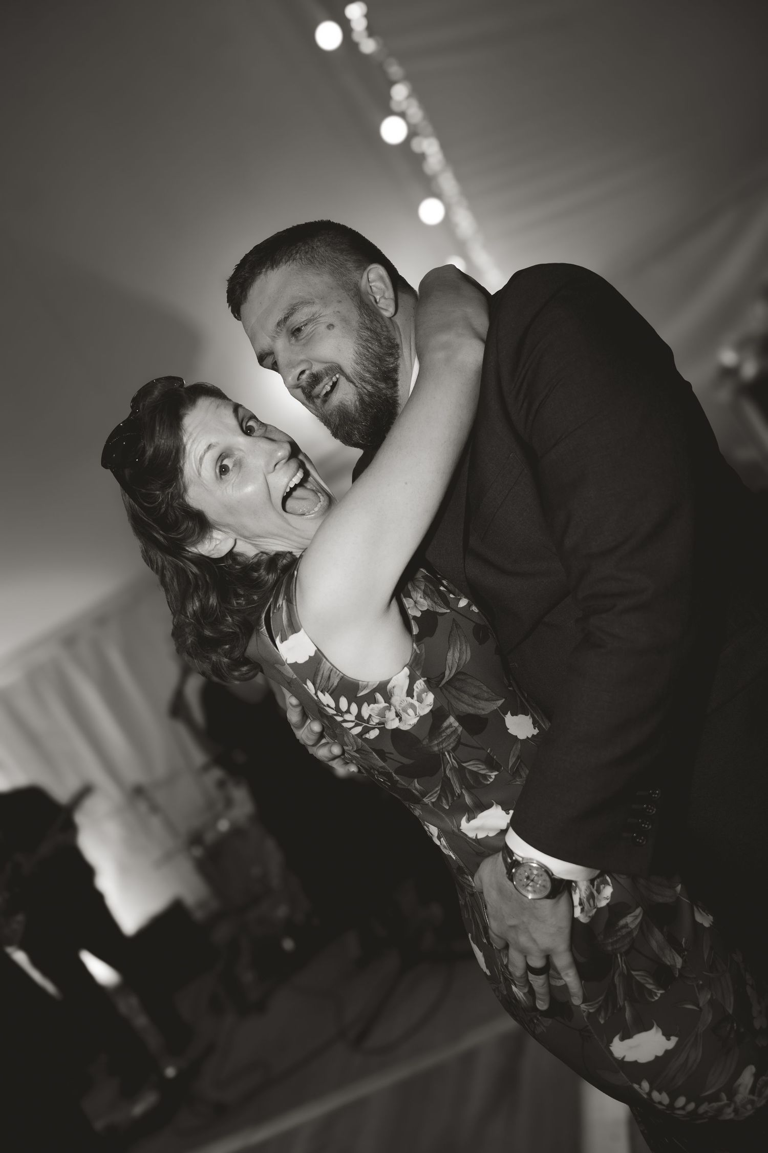 A black and white candid of a couple dancing and laughing during their wedding reception.