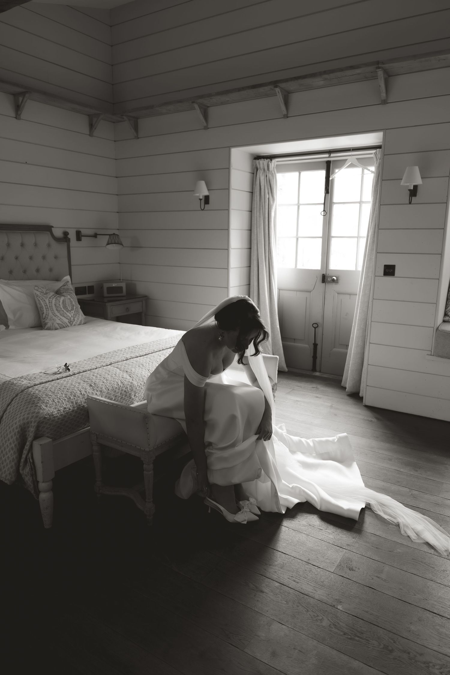 Black and white photo of a quiet moment in a rustic white bedroom with shiplap walls.