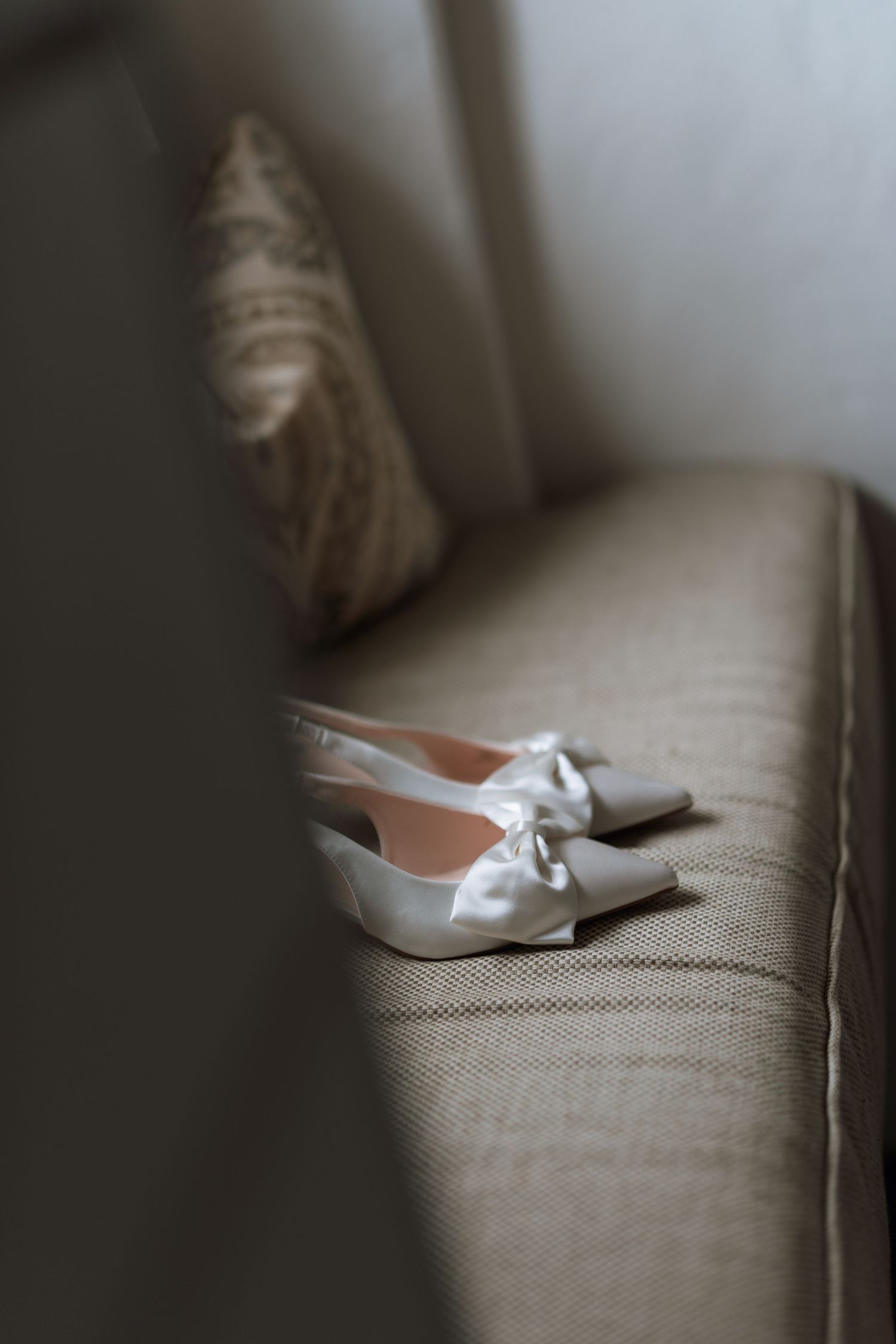 White bridal shoes with bows sit elegantly on a gray textured couch.