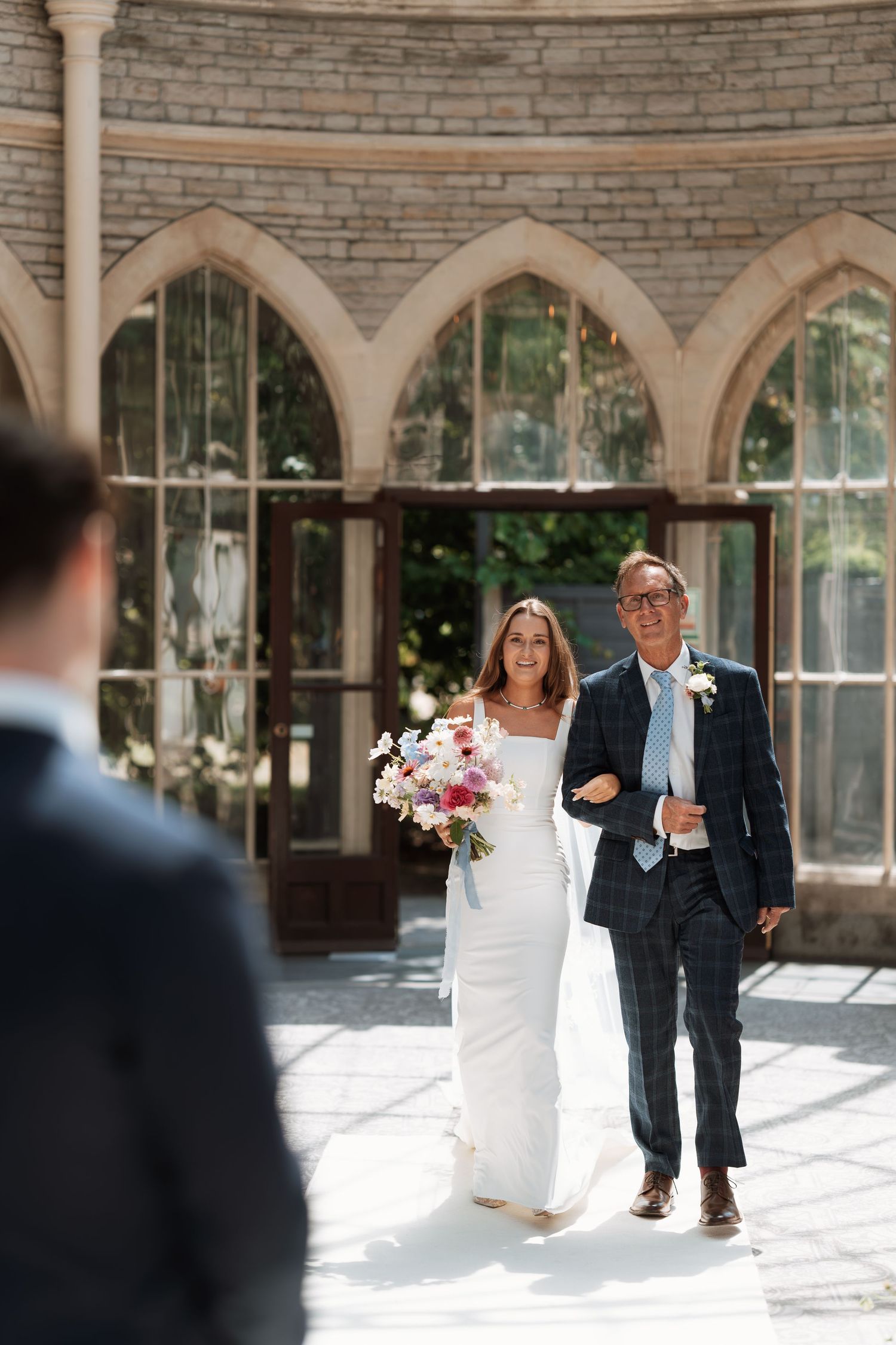 A wedding procession under beautiful stone arches with natural light streaming through.