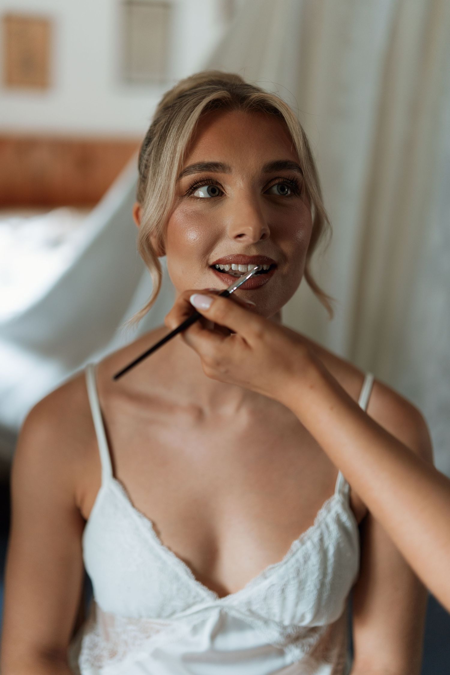 Getting ready photo of bride having makeup applied in white lingerie.