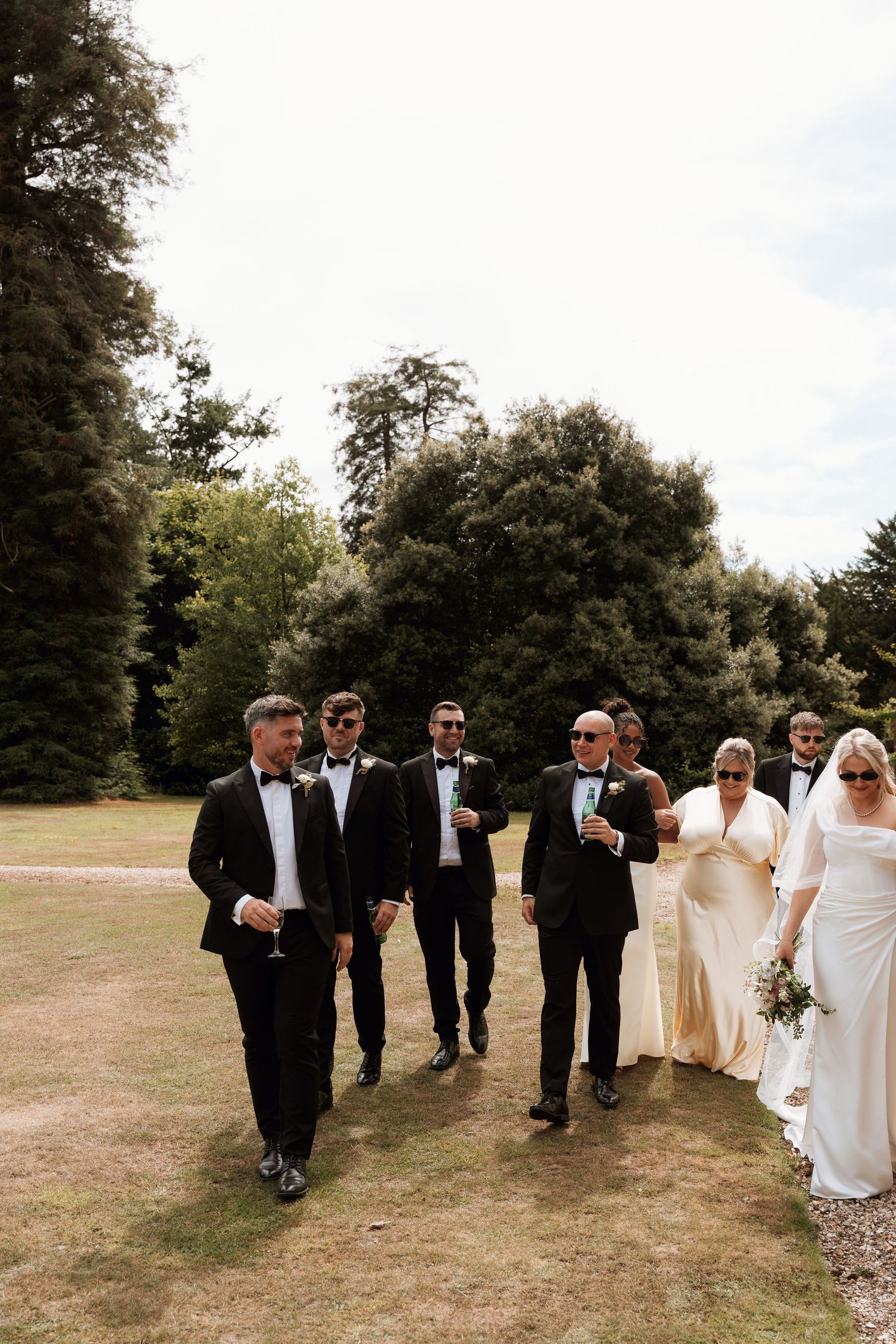 Wedding party walks together across a grassy field in elegant black and white formal attire.