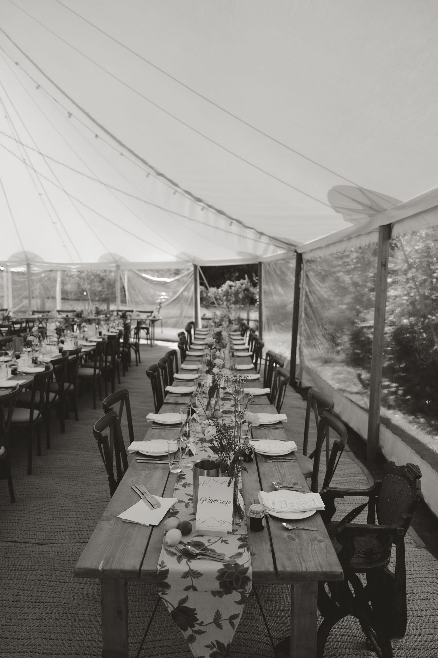 An empty wedding reception tent with elegantly set tables and chairs arranged in rows.
