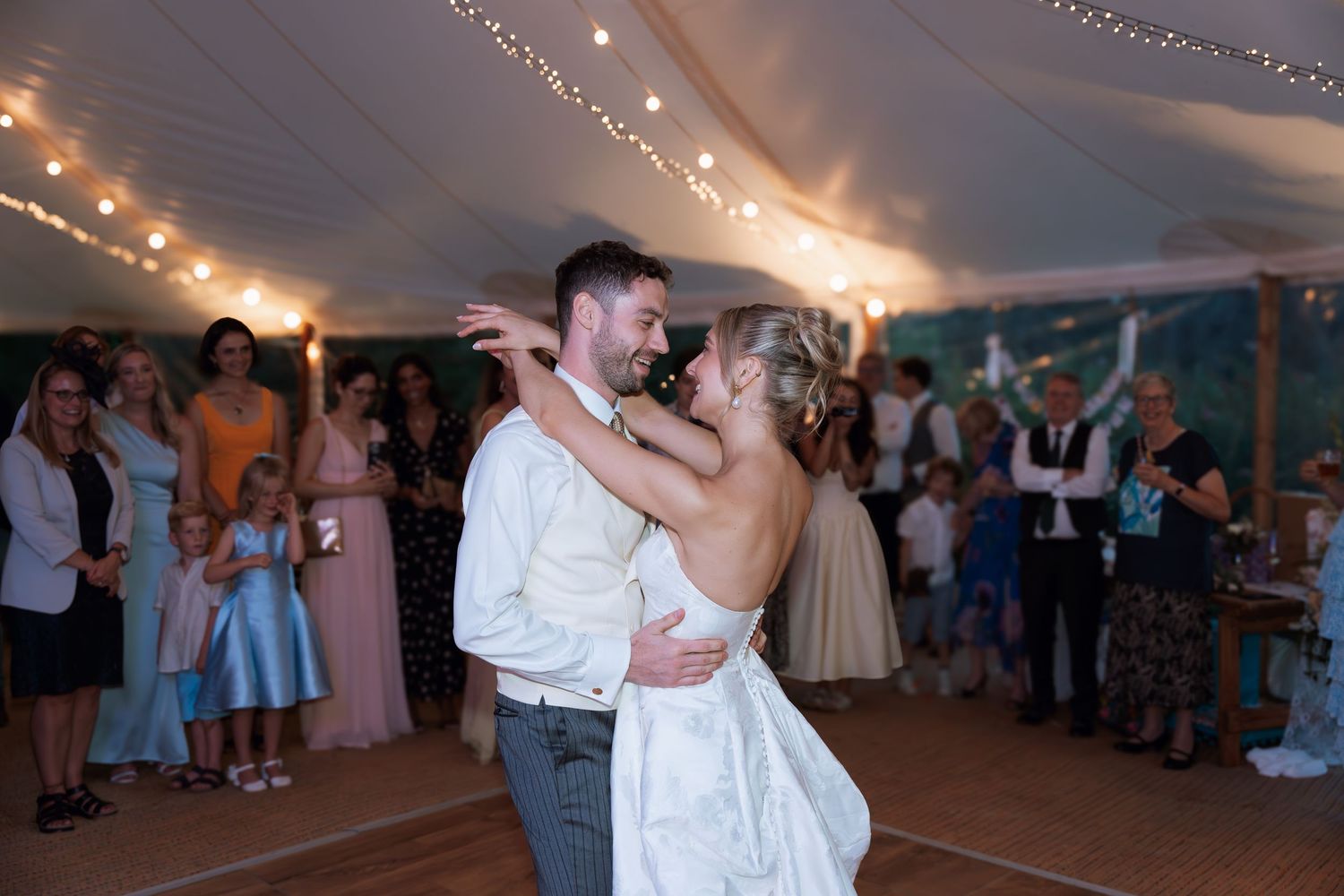 A couple shares their first dance under twinkling lights at an outdoor tented wedding reception.