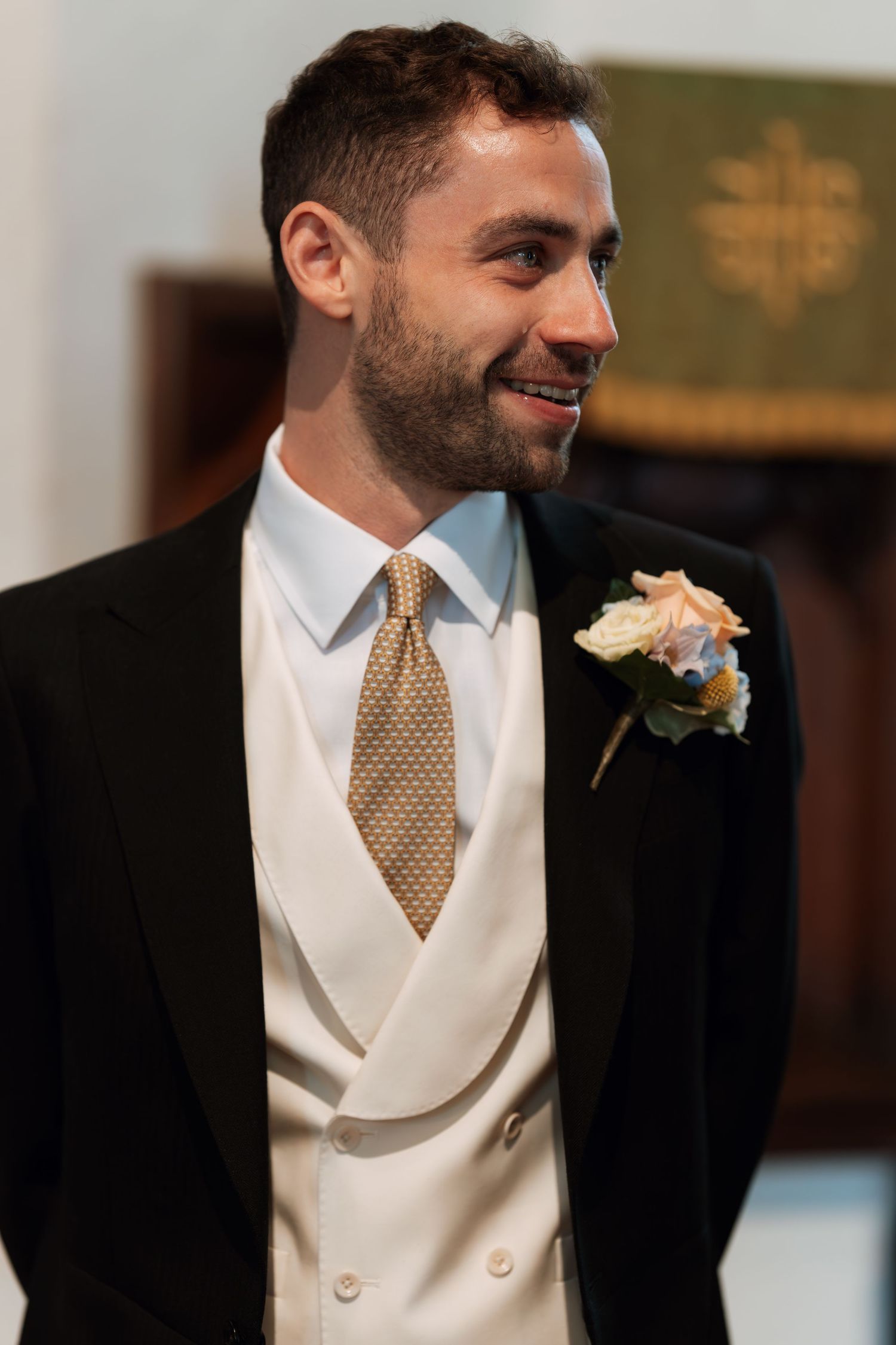 Formal attire details showing a white dress shirt with gold tie and cream vest at a wedding.