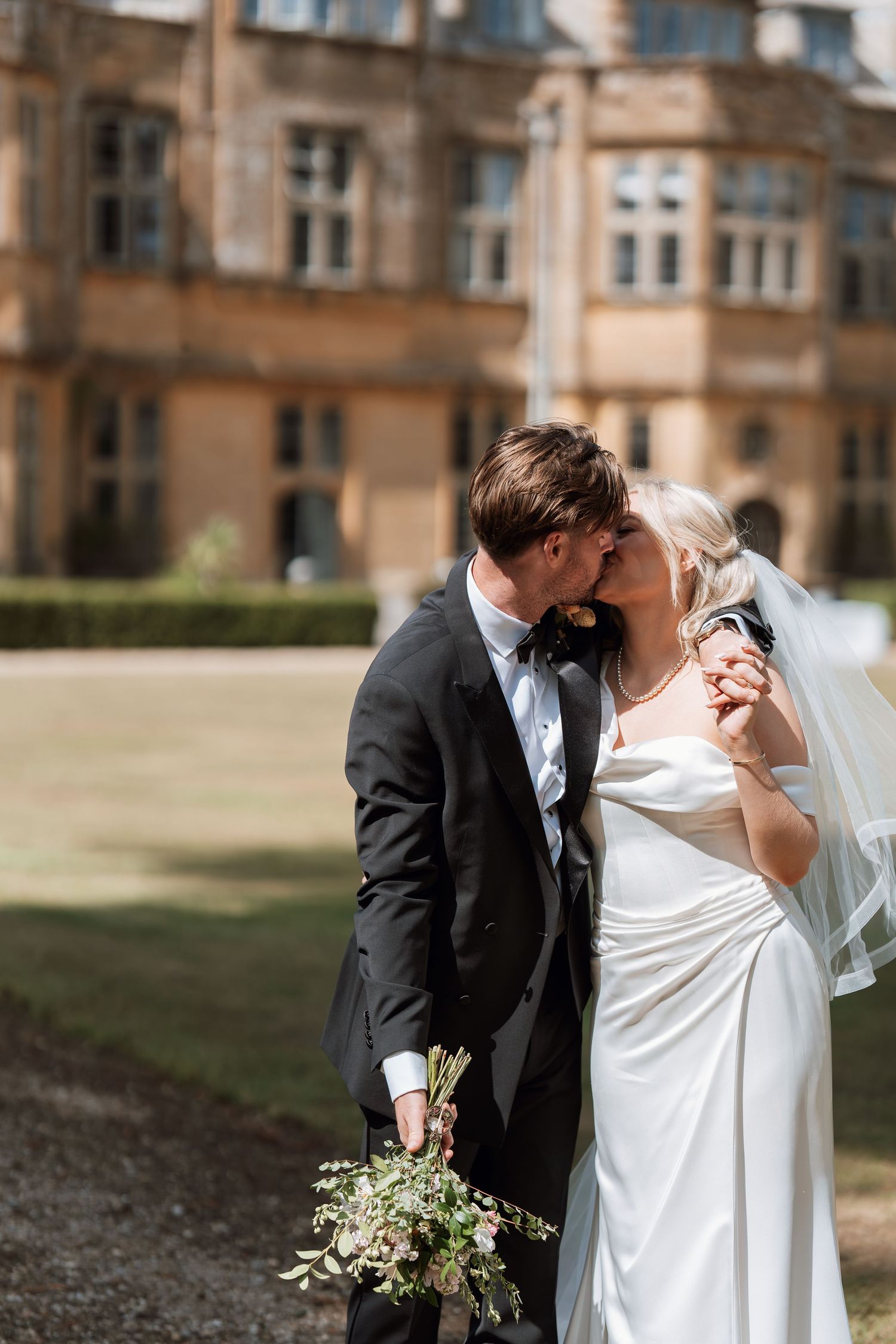 A romantic wedding moment captured in front of a grand stone building with a delicate bridal bouquet.