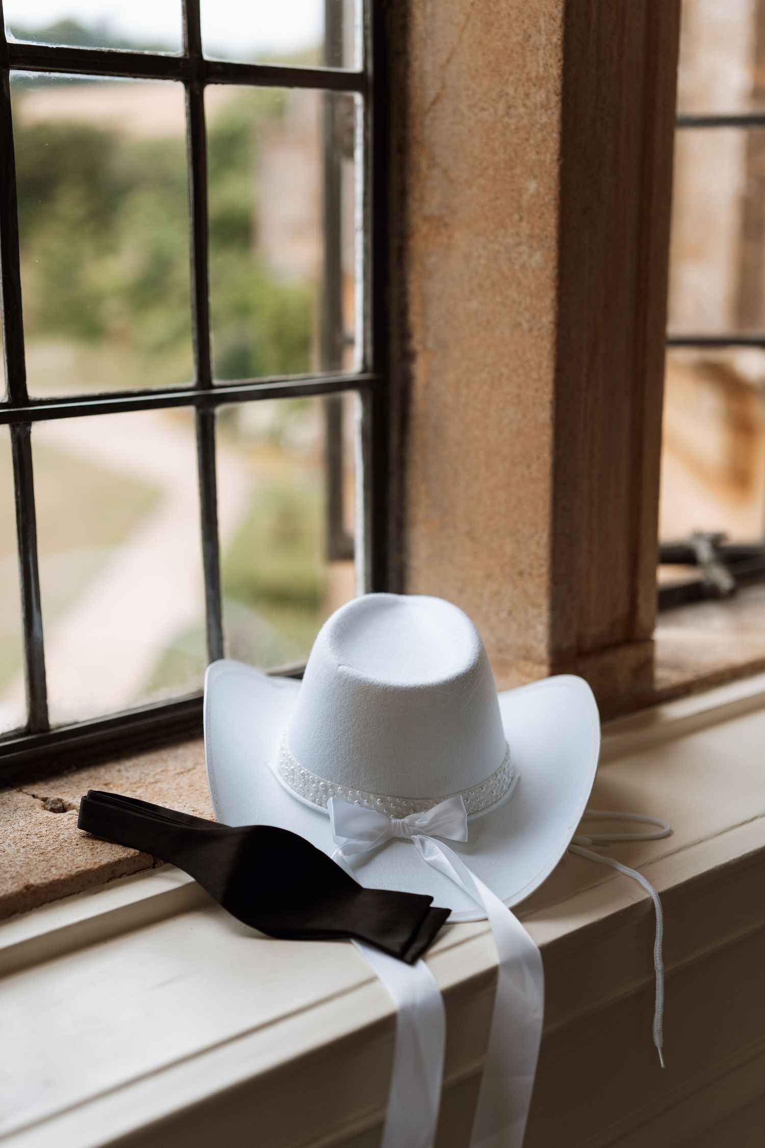 A white cowboy hat with lace trim sits on a rustic windowsill in natural light.
