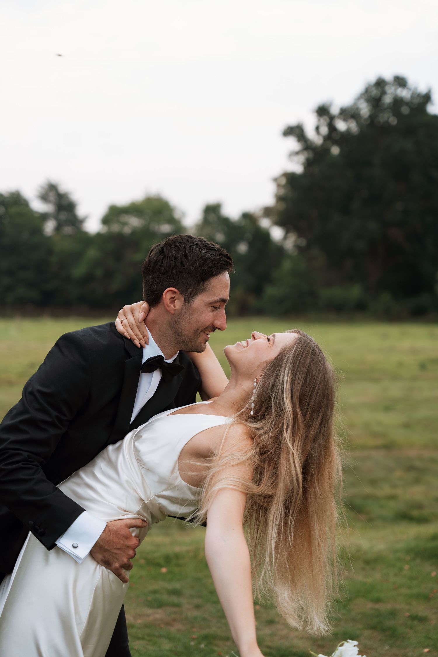 Couple in wedding attire share romantic dip pose in grassy field.