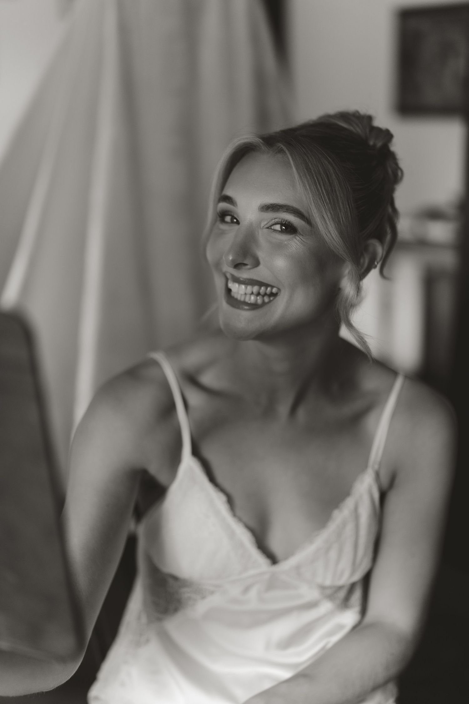 Black and white portrait of a smiling person in a white camisole with an elegant updo hairstyle.