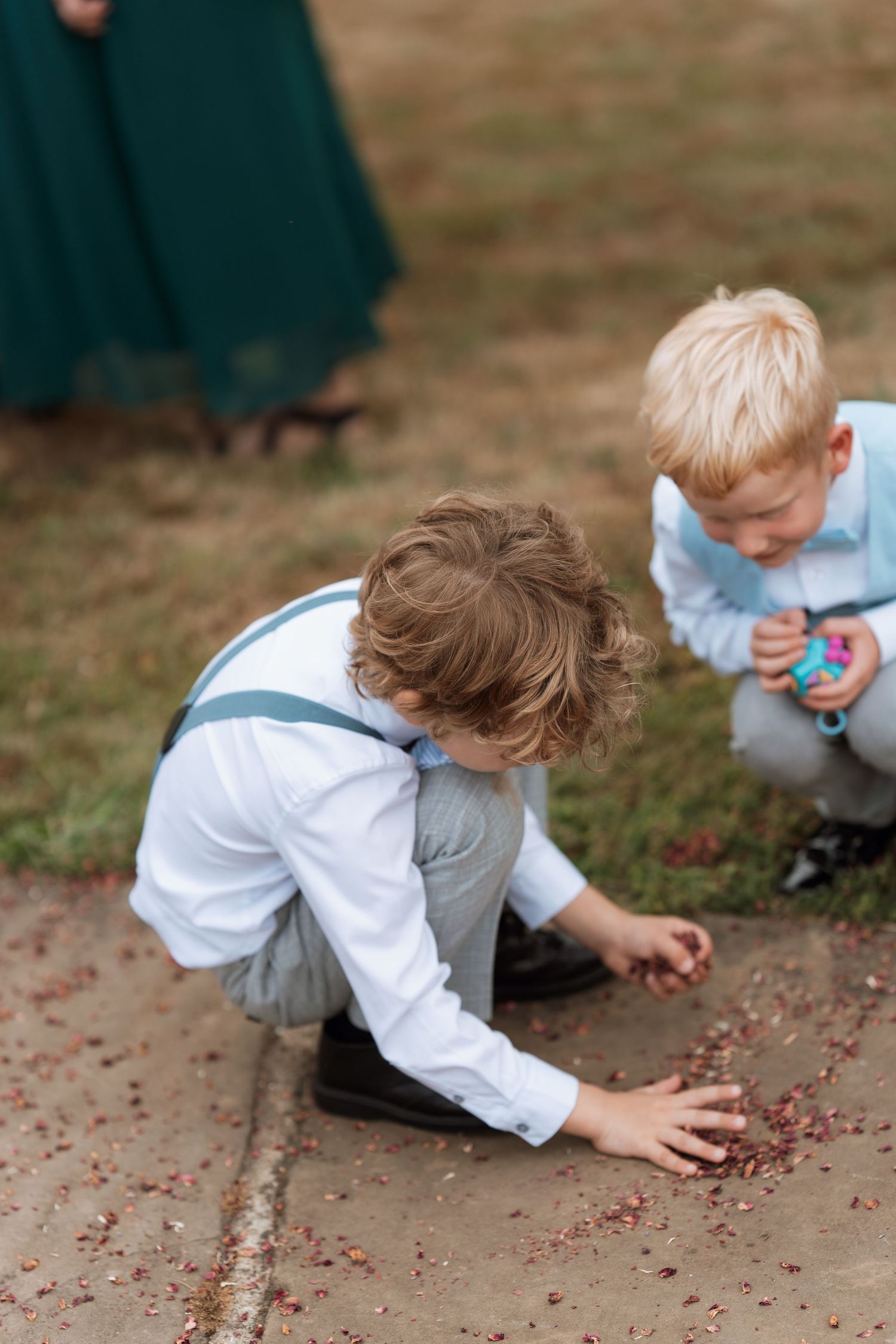 Young children in formal attire gather scattered petals from the ground at a wedding.