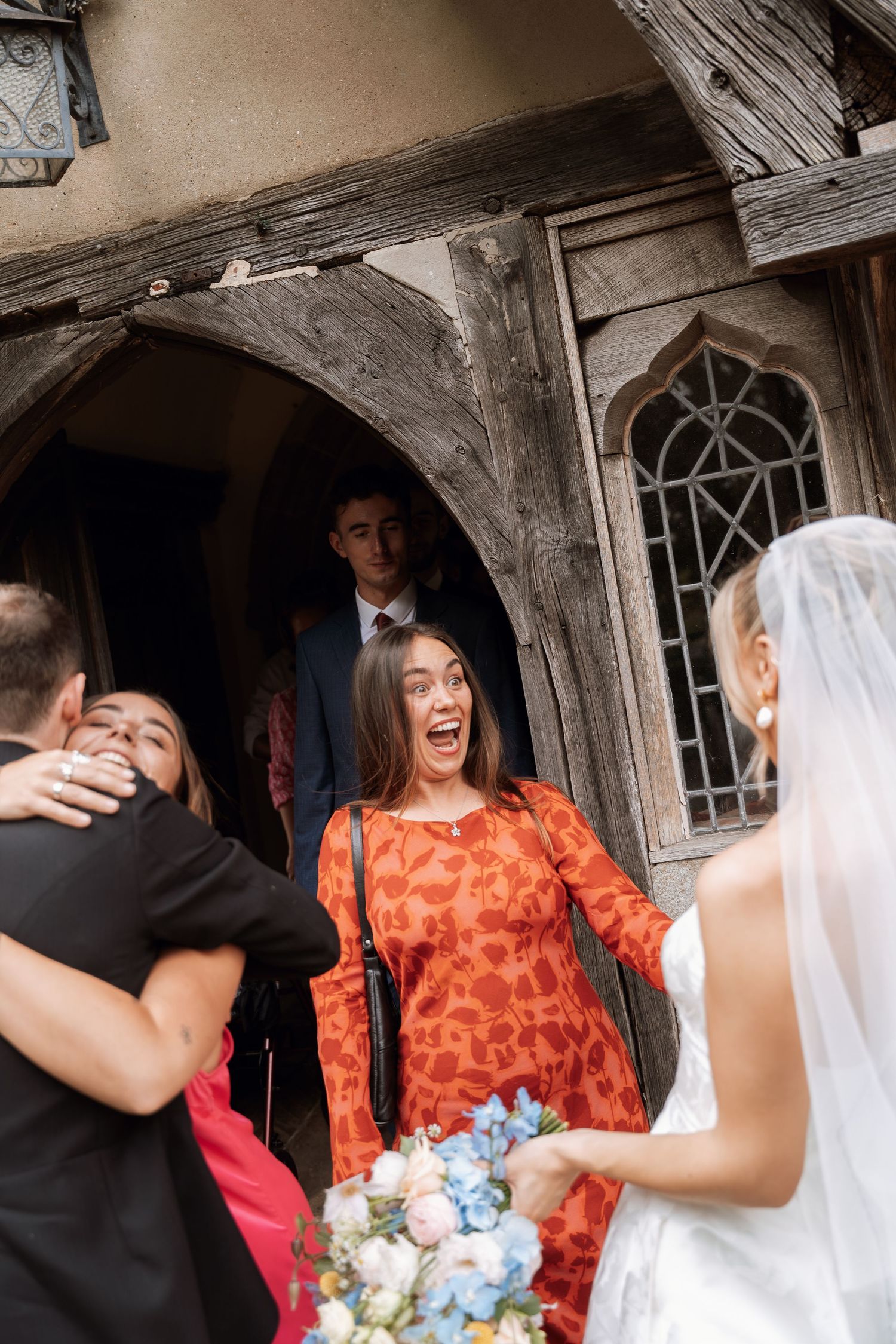 A joyful wedding scene with laughter and embraces in front of a rustic wooden building.