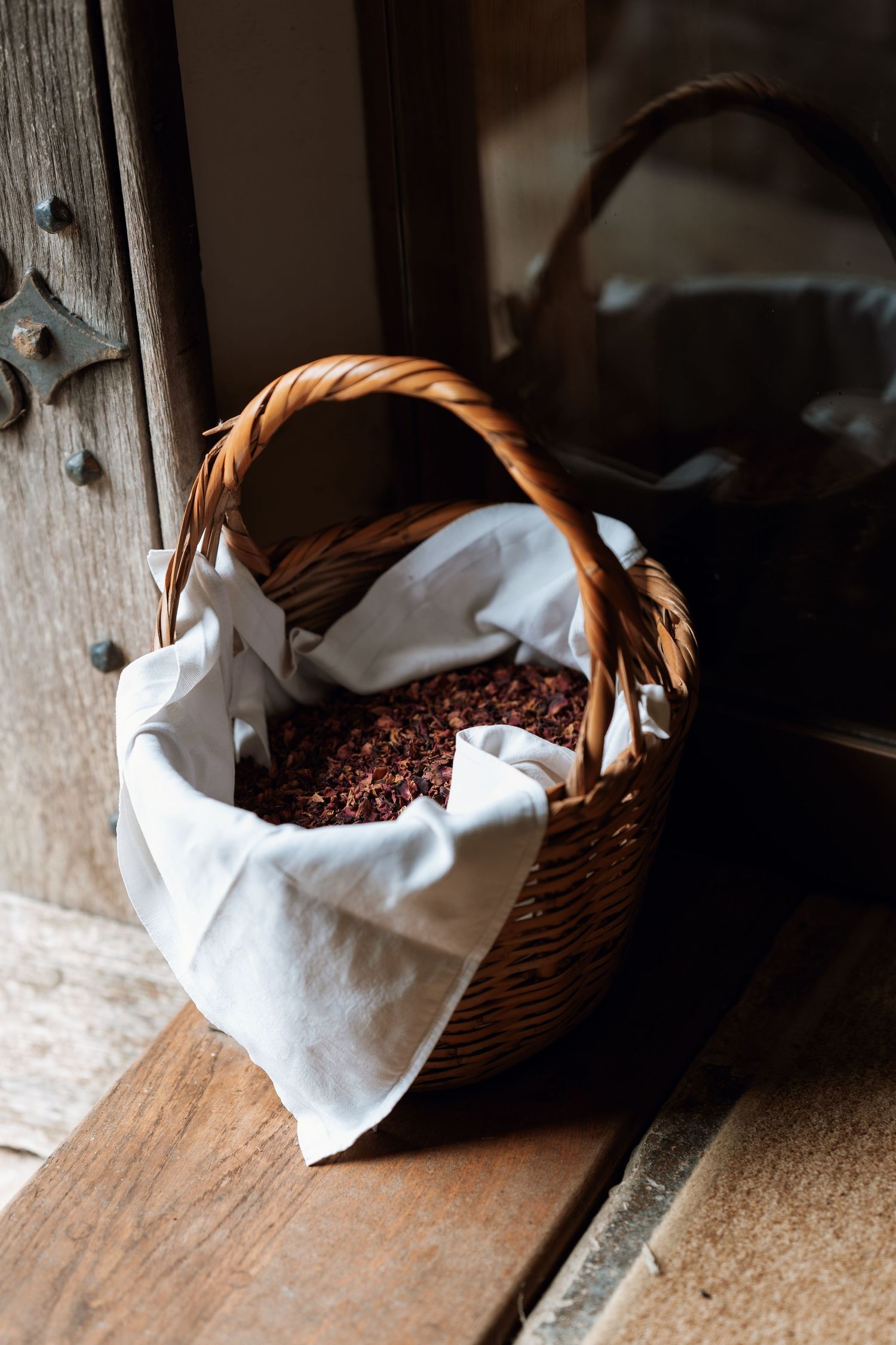 A rustic wicker basket lined with white cloth holds flower petals for a wedding ceremony.