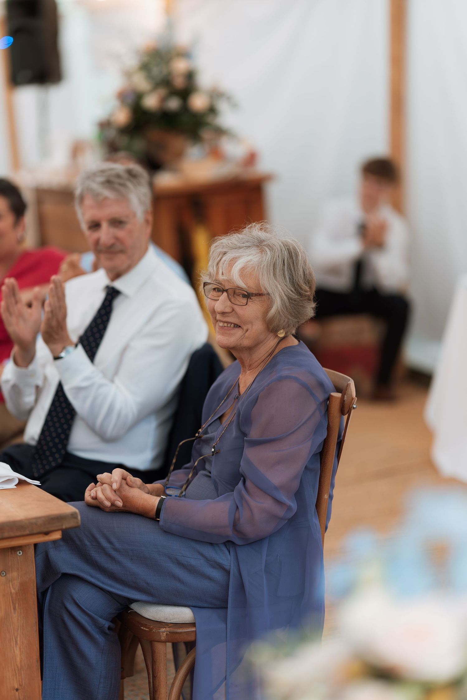 A guest in a blue outfit smiles during a wedding reception in an elegant tent setting.
