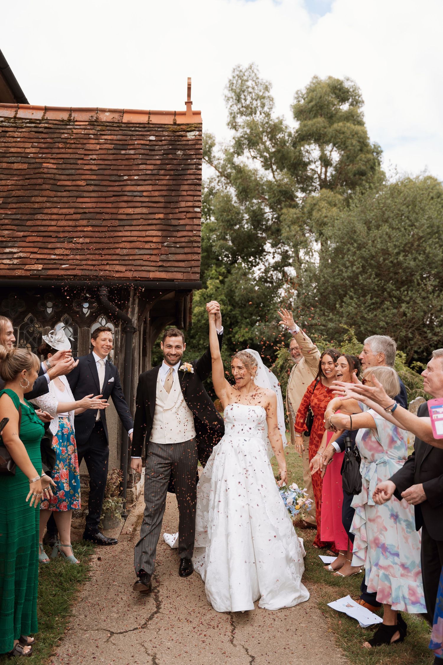 Newlyweds exit their wedding celebration through a crowd of cheering guests throwing confetti.