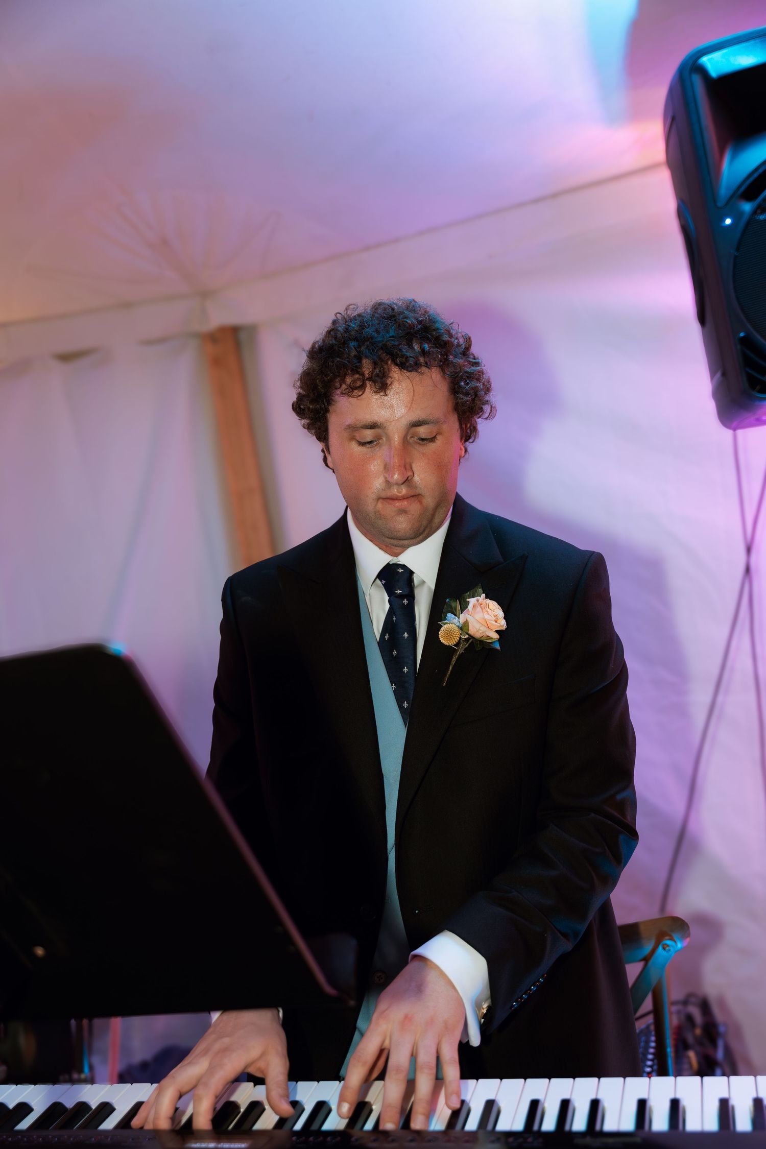 Musician playing piano at wedding reception with purple lighting ambiance.