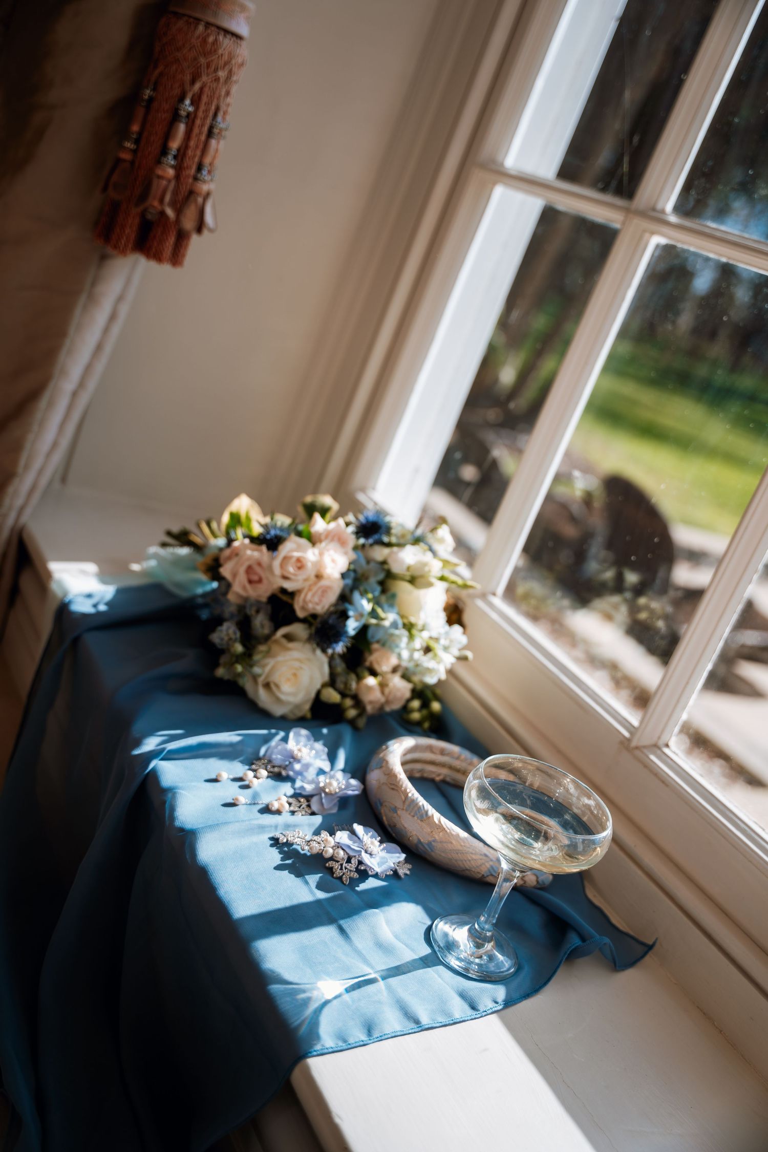 Wedding decor detail featuring blue tablecloth with romantic floral arrangements by a window.