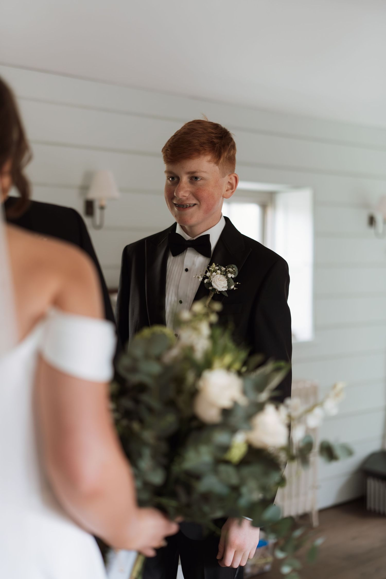 An intimate first look moment in a bright white-walled room with natural window light.