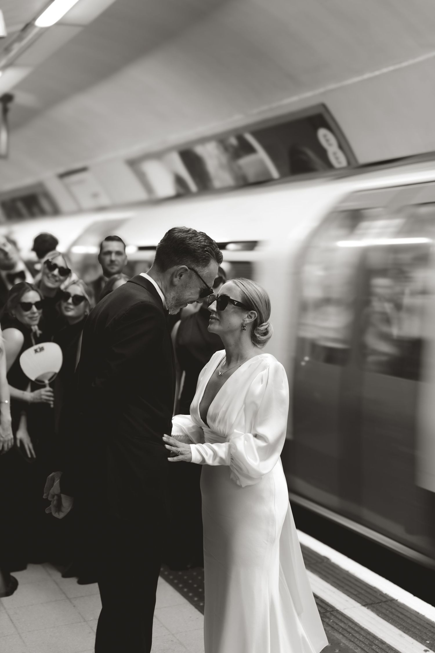 A romantic black and white wedding photo of a couple sharing an intimate moment on a subway platform.