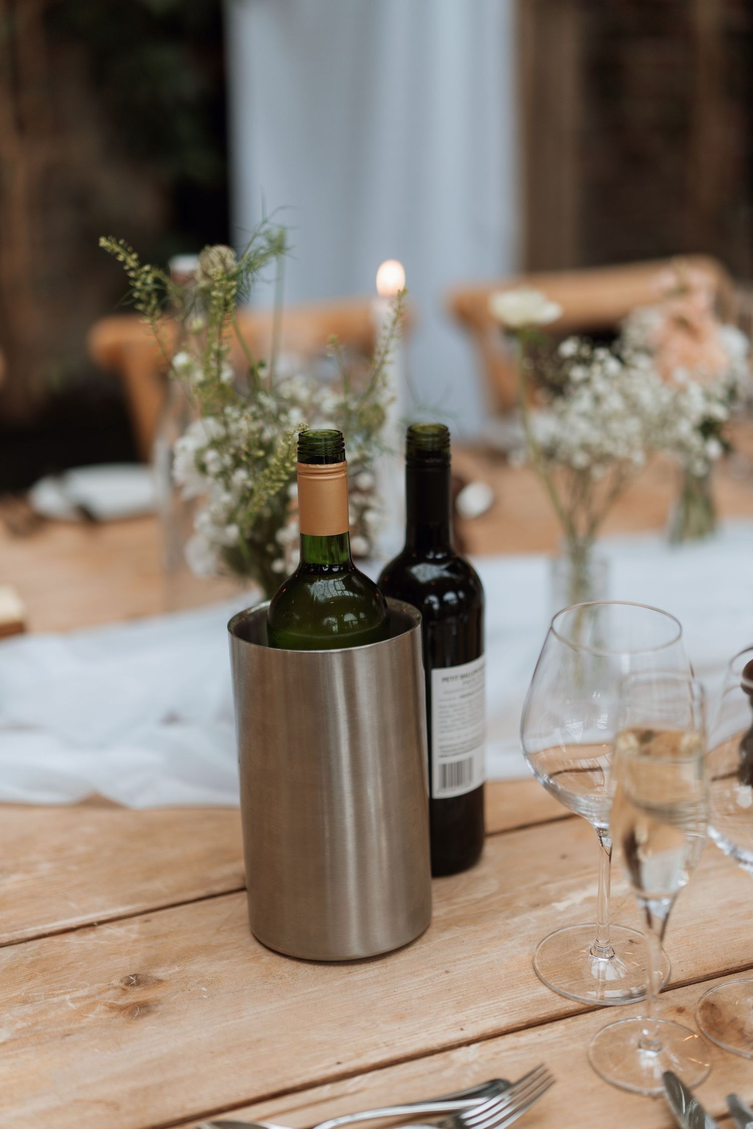 Wedding table details with wine bottles and delicate floral arrangements on wooden surface.