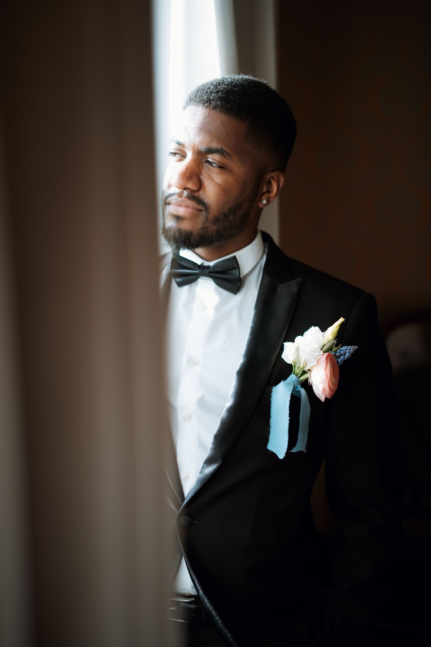 A formal portrait featuring a classic black tuxedo with bow tie and floral boutonniere.