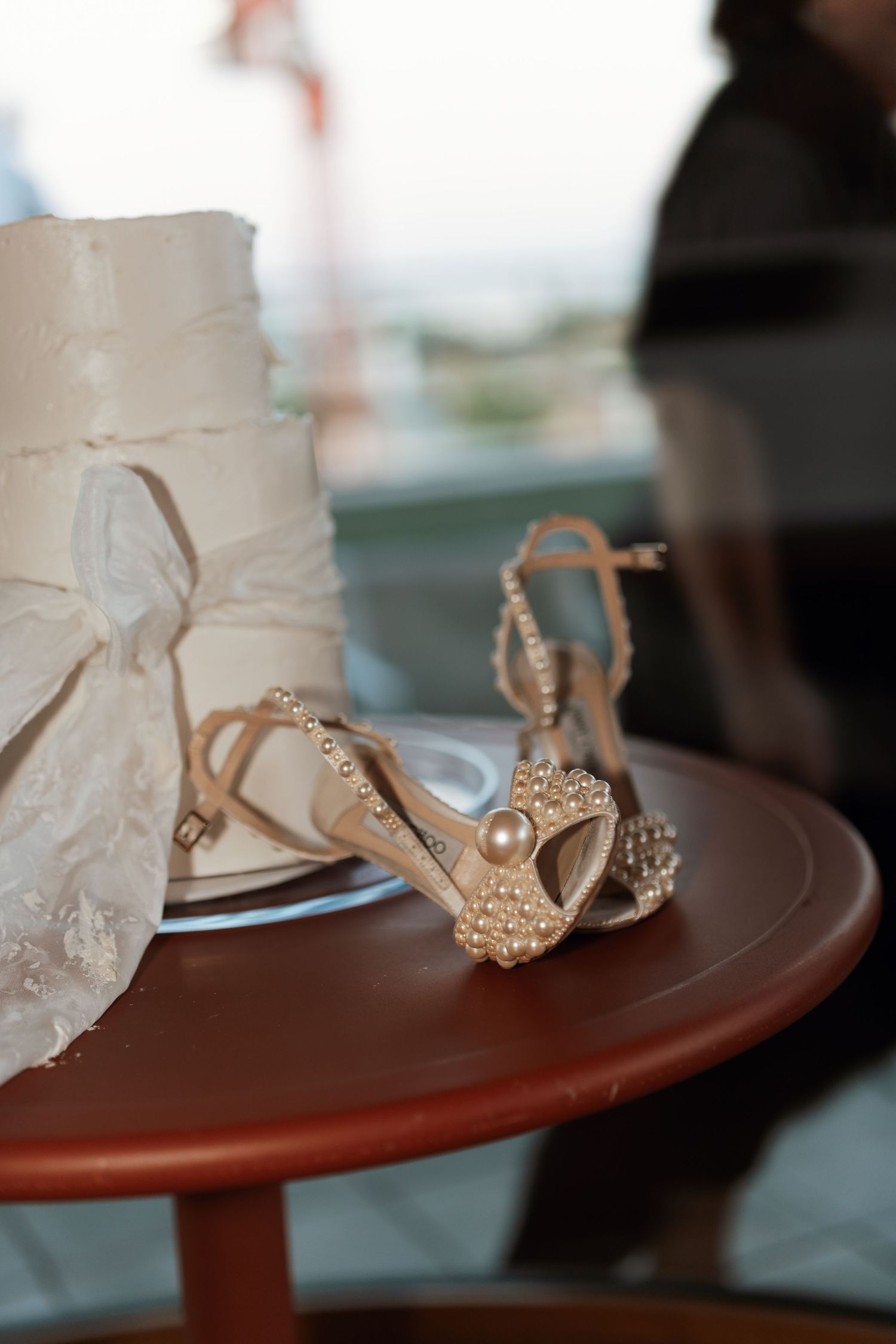 Wedding accessories featuring delicate beaded sandals next to white cake layers on a round table.
