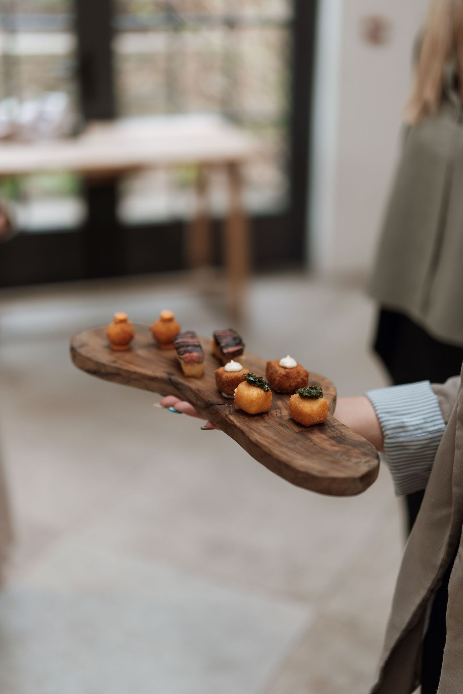 Wooden serving board with small appetizers being presented at an event.