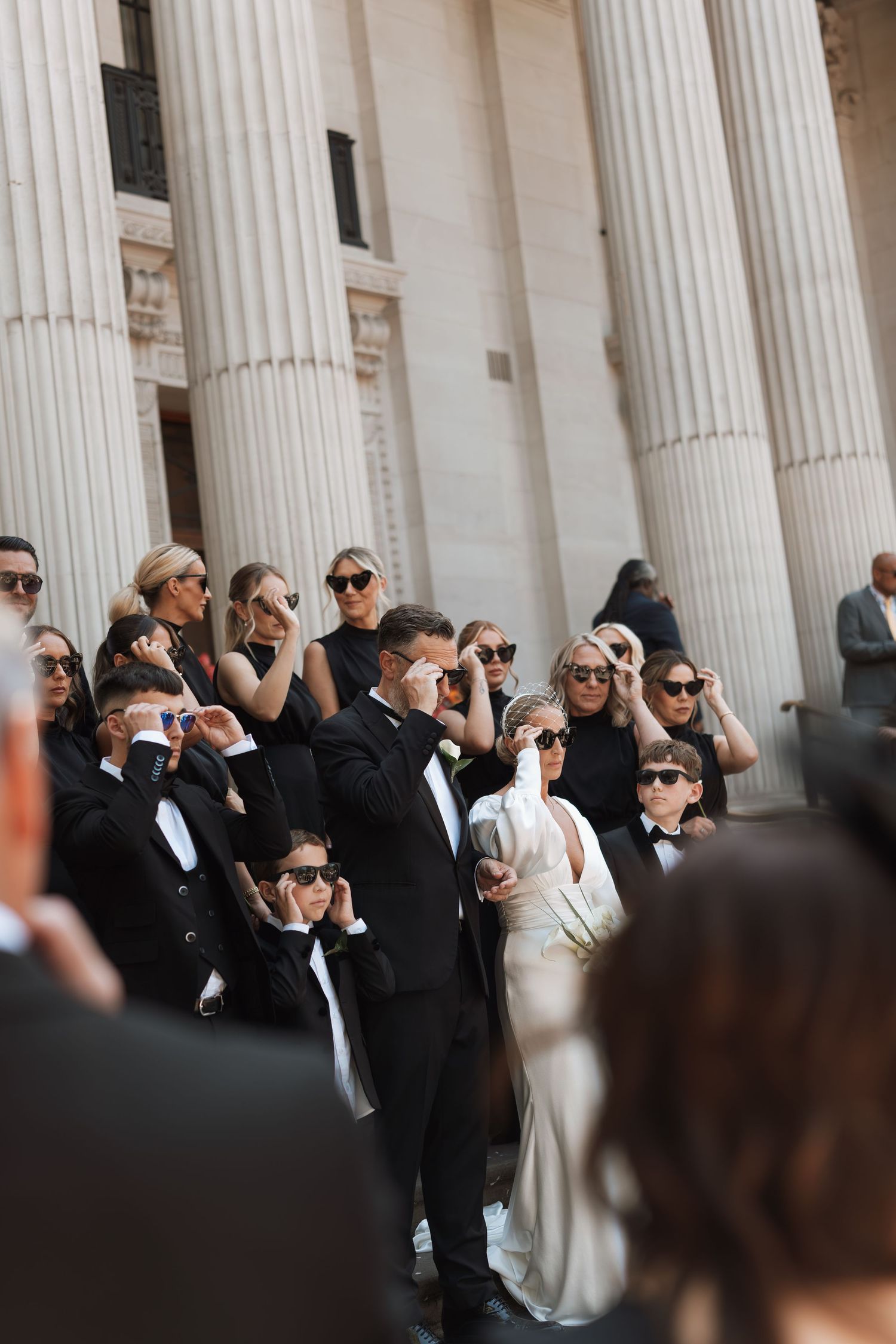 Wedding party in formal black attire gathering between classic white columns.