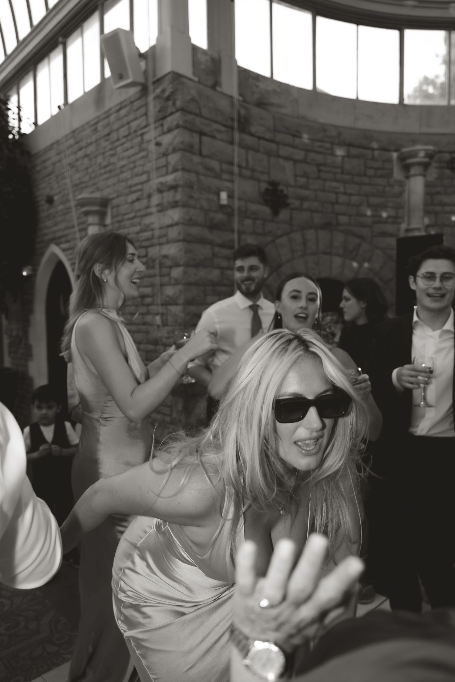 Wedding guests dancing and celebrating at a lively party with brick walls and festive lighting.