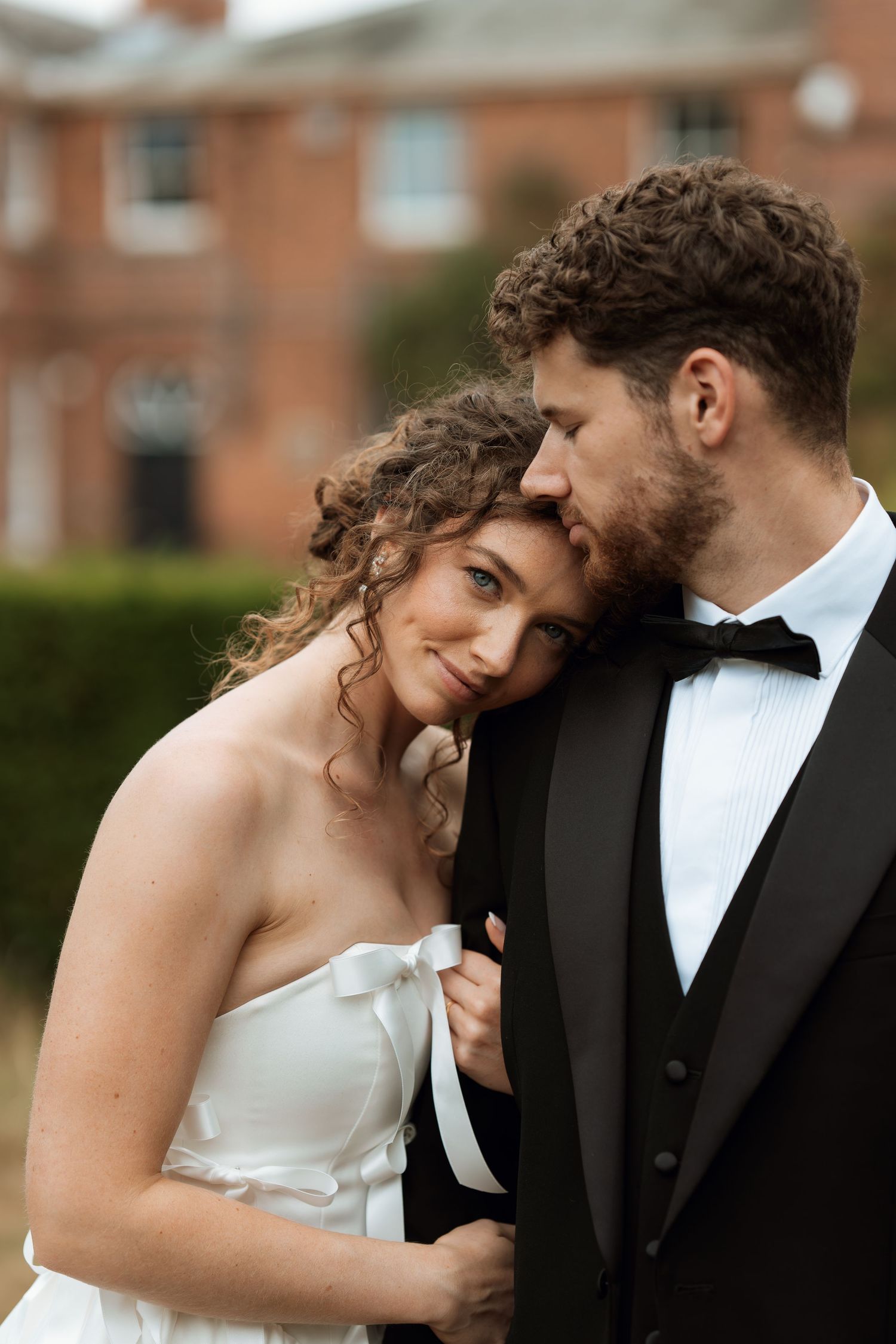 Intimate moment between newlyweds posing against brick building backdrop.