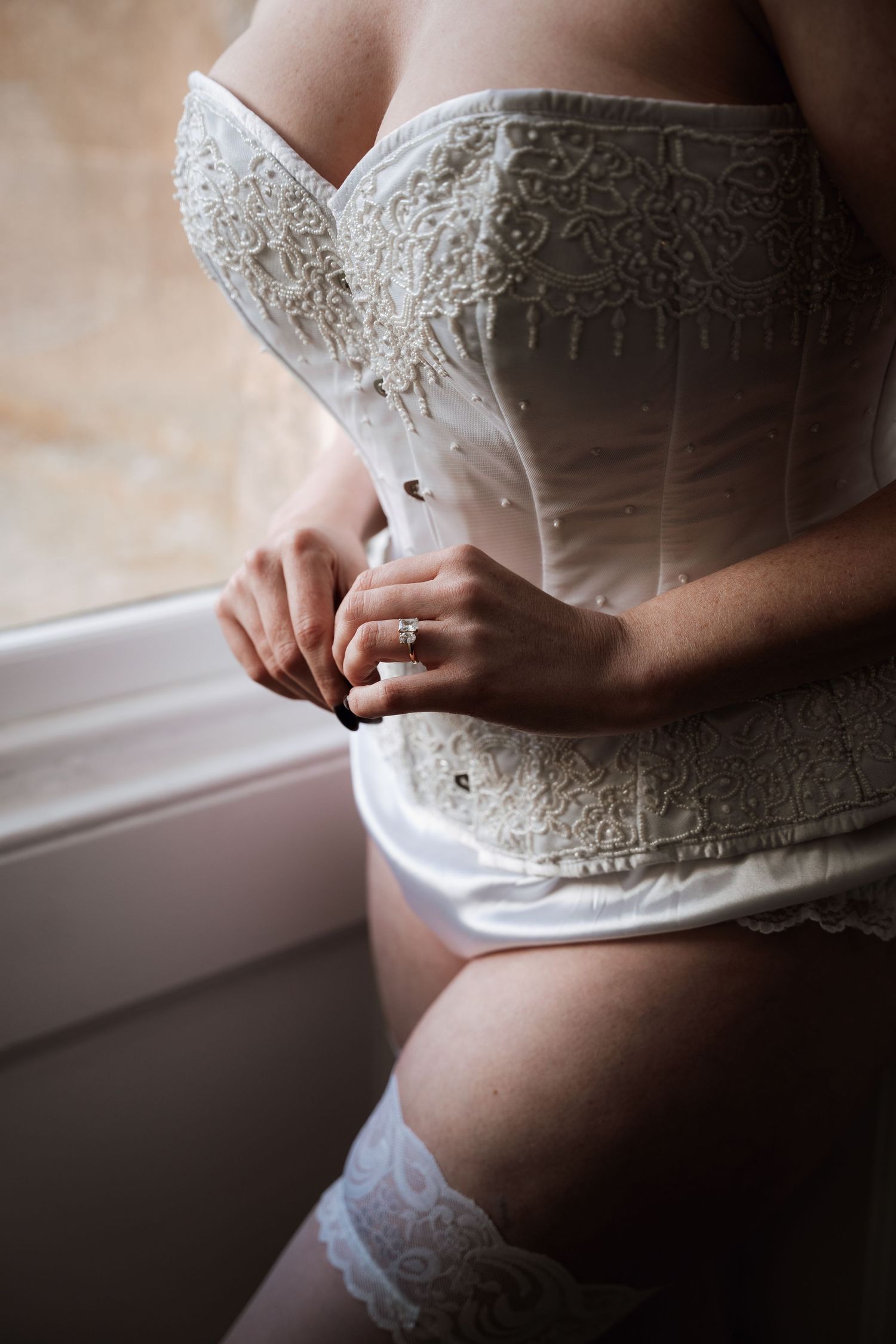 Close-up detail of lace wedding corset and hands wearing ring.
