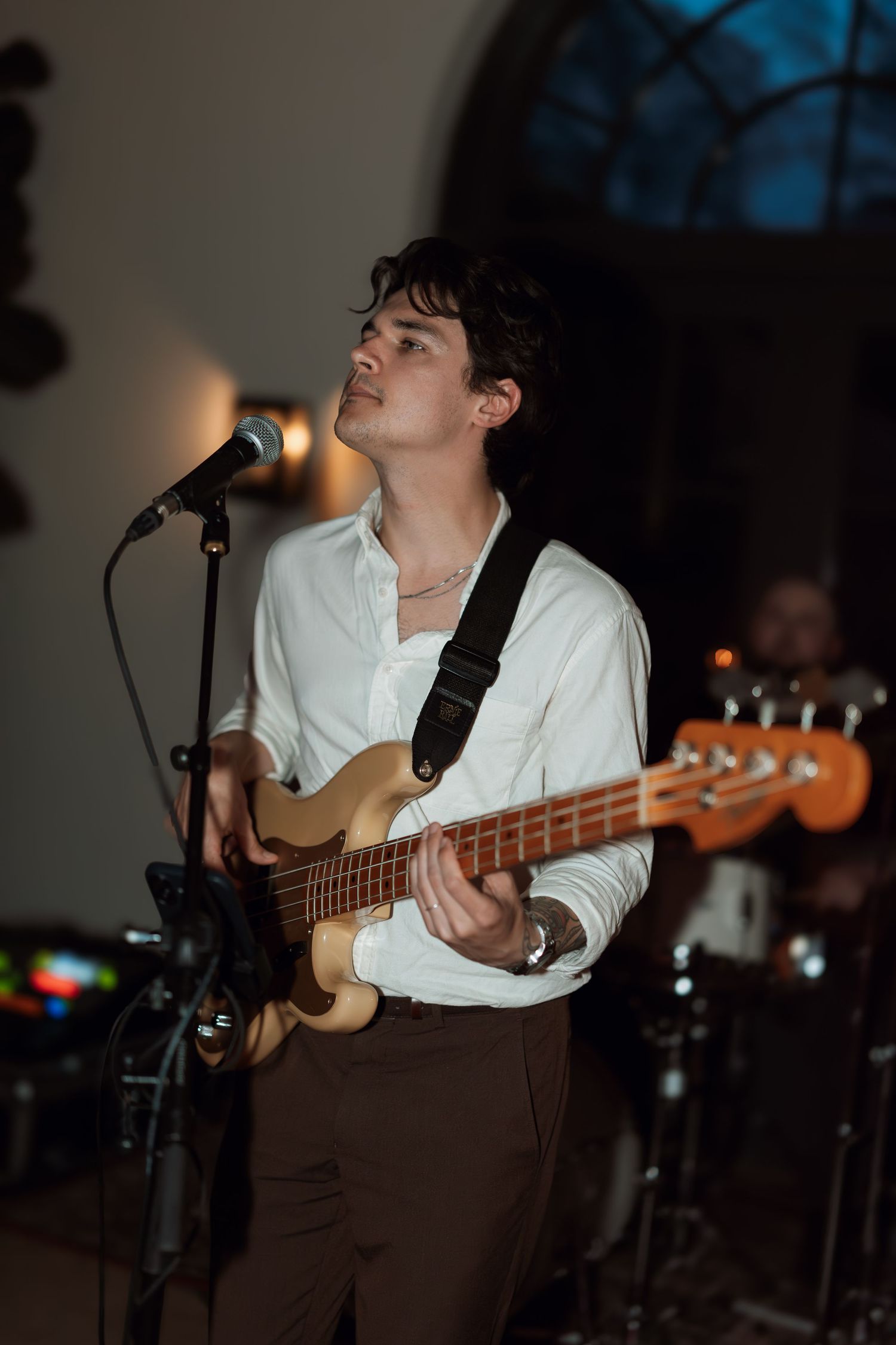 Musician playing bass guitar while singing into microphone during evening performance.