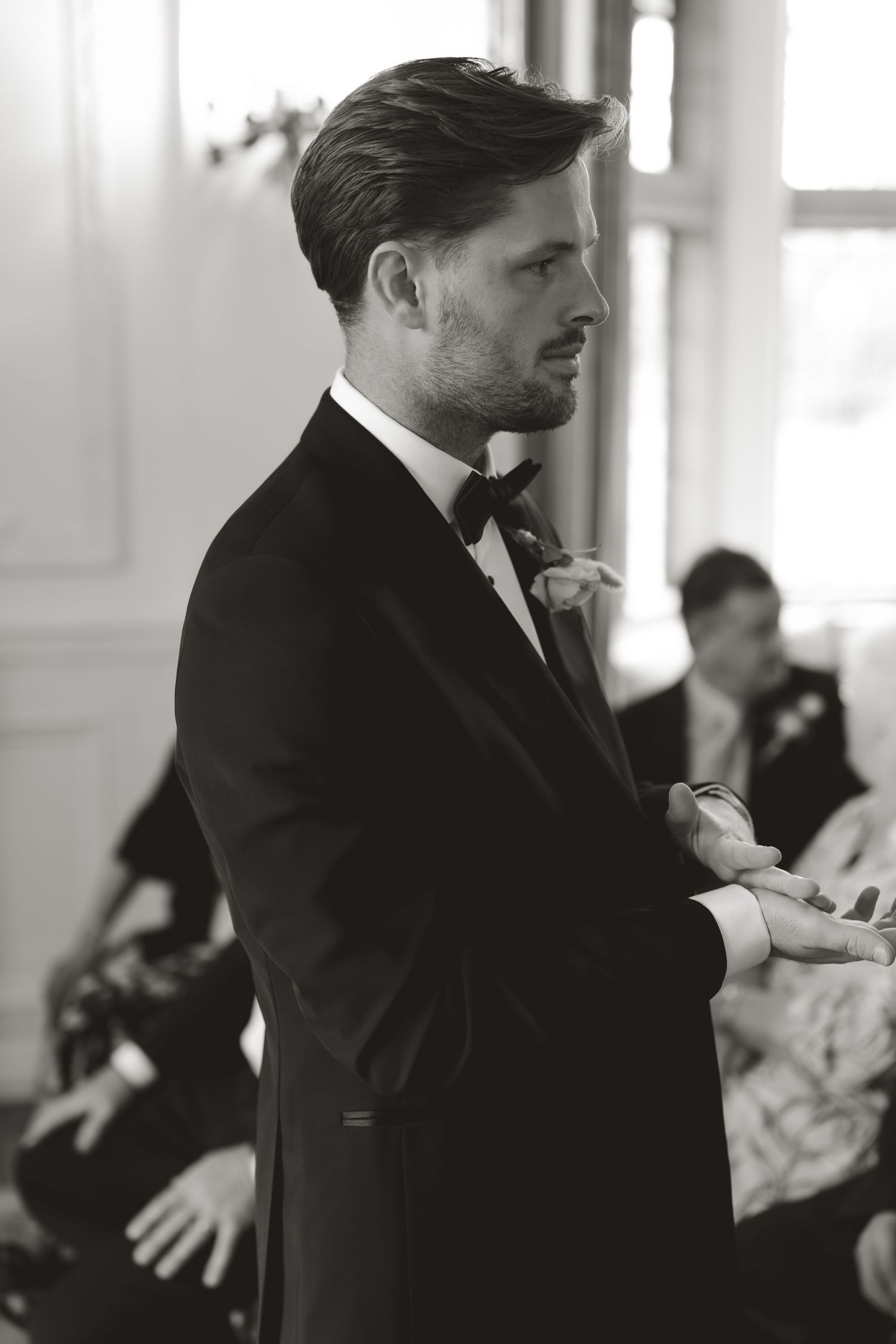 Black and white portrait of a person in a formal tuxedo and bowtie adjusting their cuffs before an event.