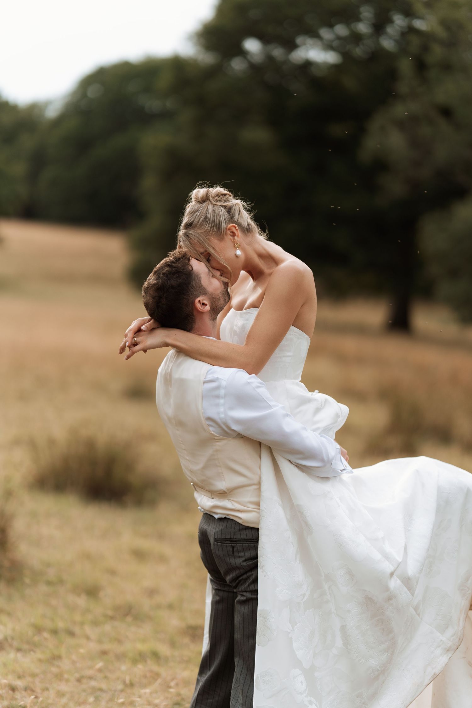 A joyful wedding couple embracing in a golden field during their countryside celebration.