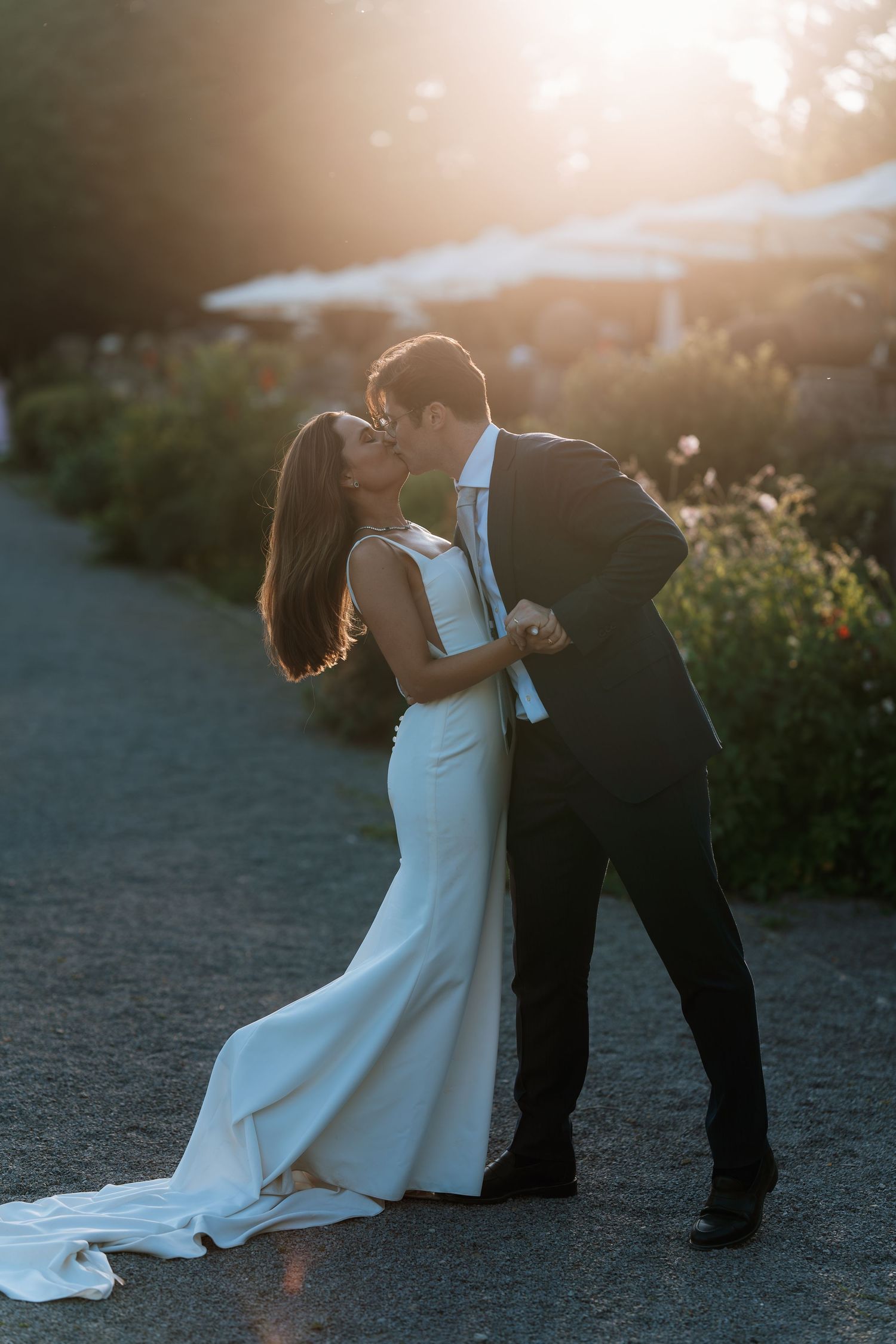 A romantic sunset kiss between newlyweds in formal attire.