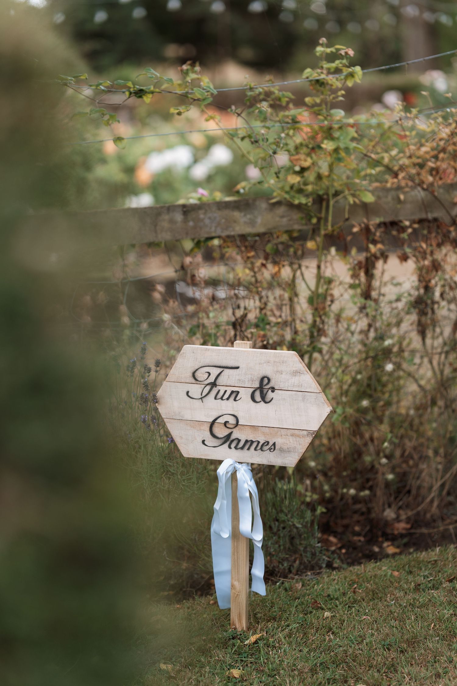 A wooden directional sign reading 'Fun & Games' with light blue ribbons in a garden setting.