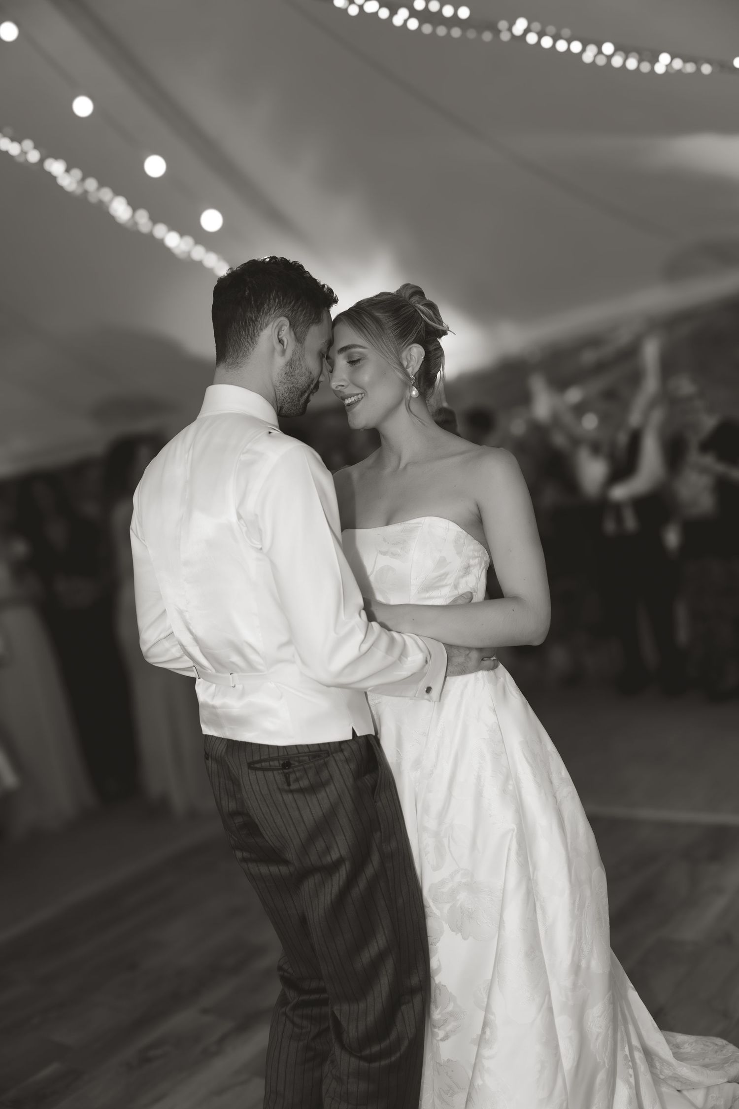 A romantic first dance between newlyweds at their wedding reception under twinkling lights.
