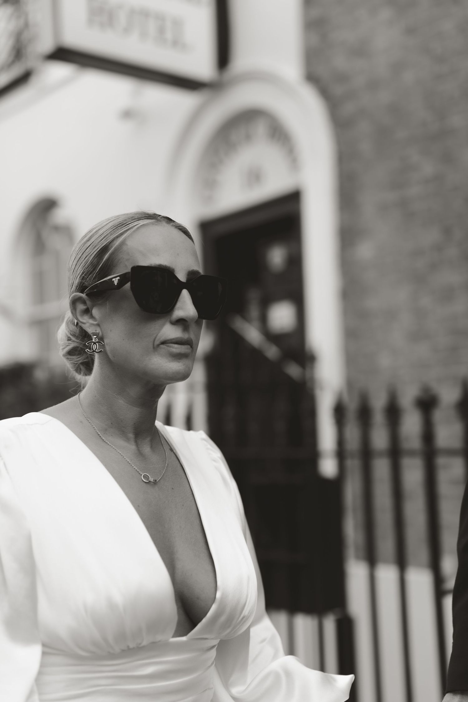 Elegant bride in a white plunging neckline dress and sunglasses poses on a city street.