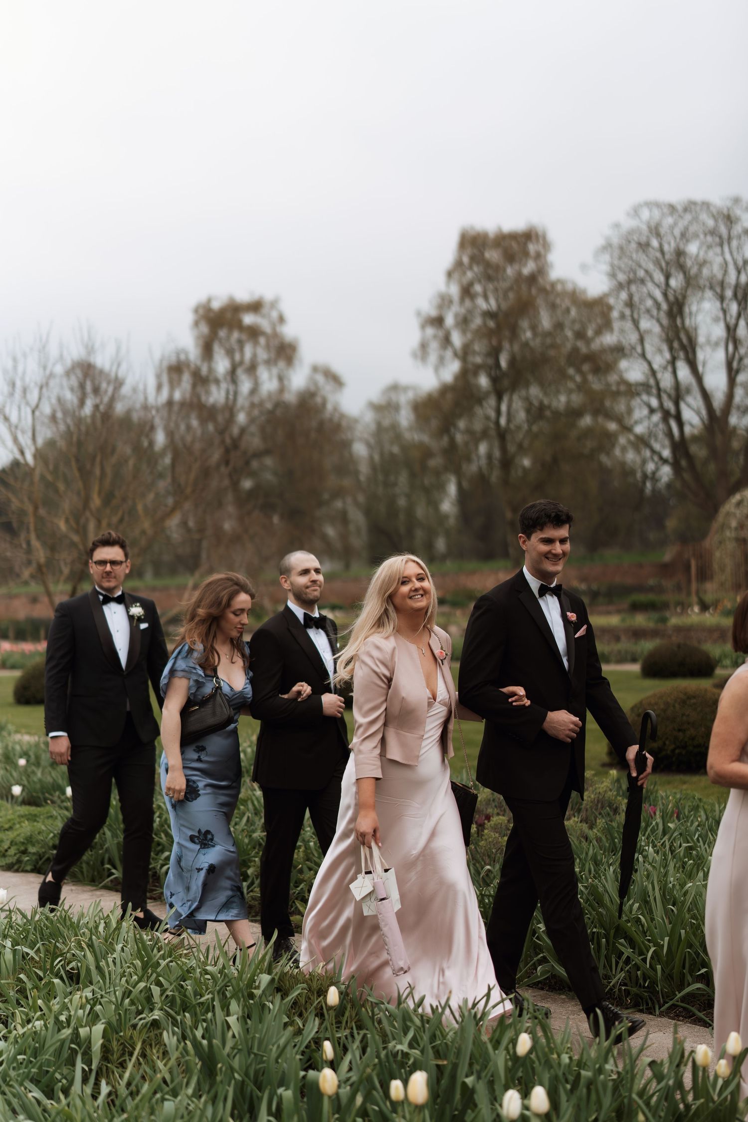 Wedding party walking outdoors in formalwear with bridesmaids in blush dresses.