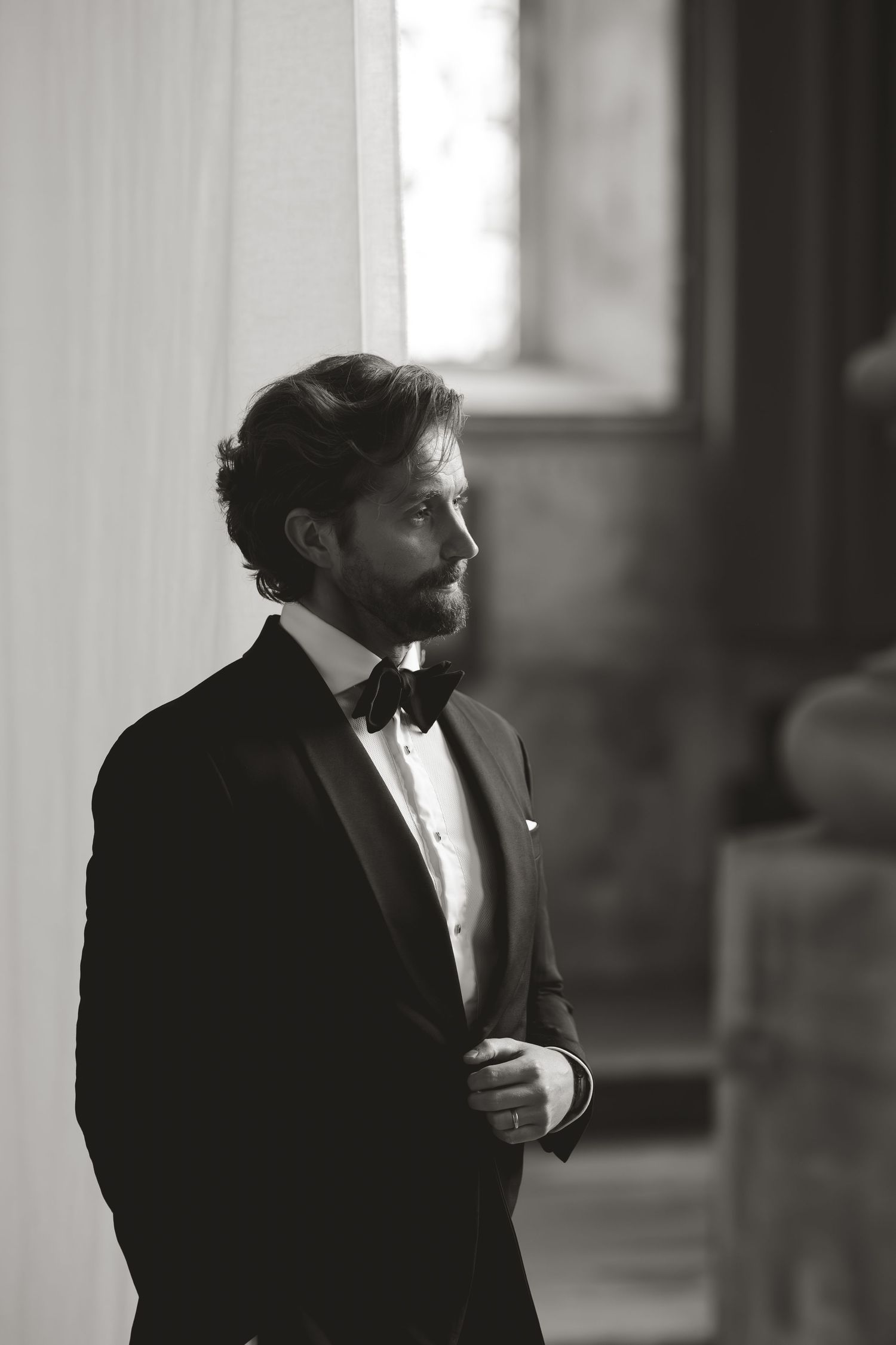 Side view portrait of man in formal black tie attire against white wall.