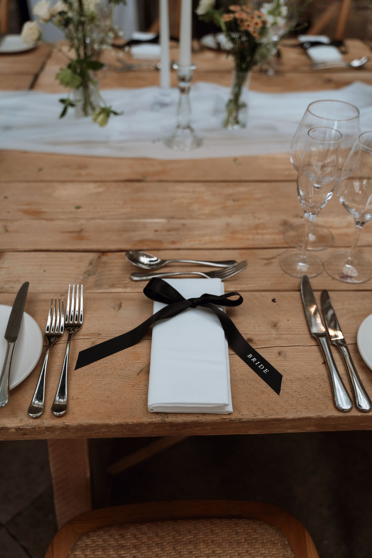 Elegant place setting with white napkin tied with black ribbon on rustic wooden table.