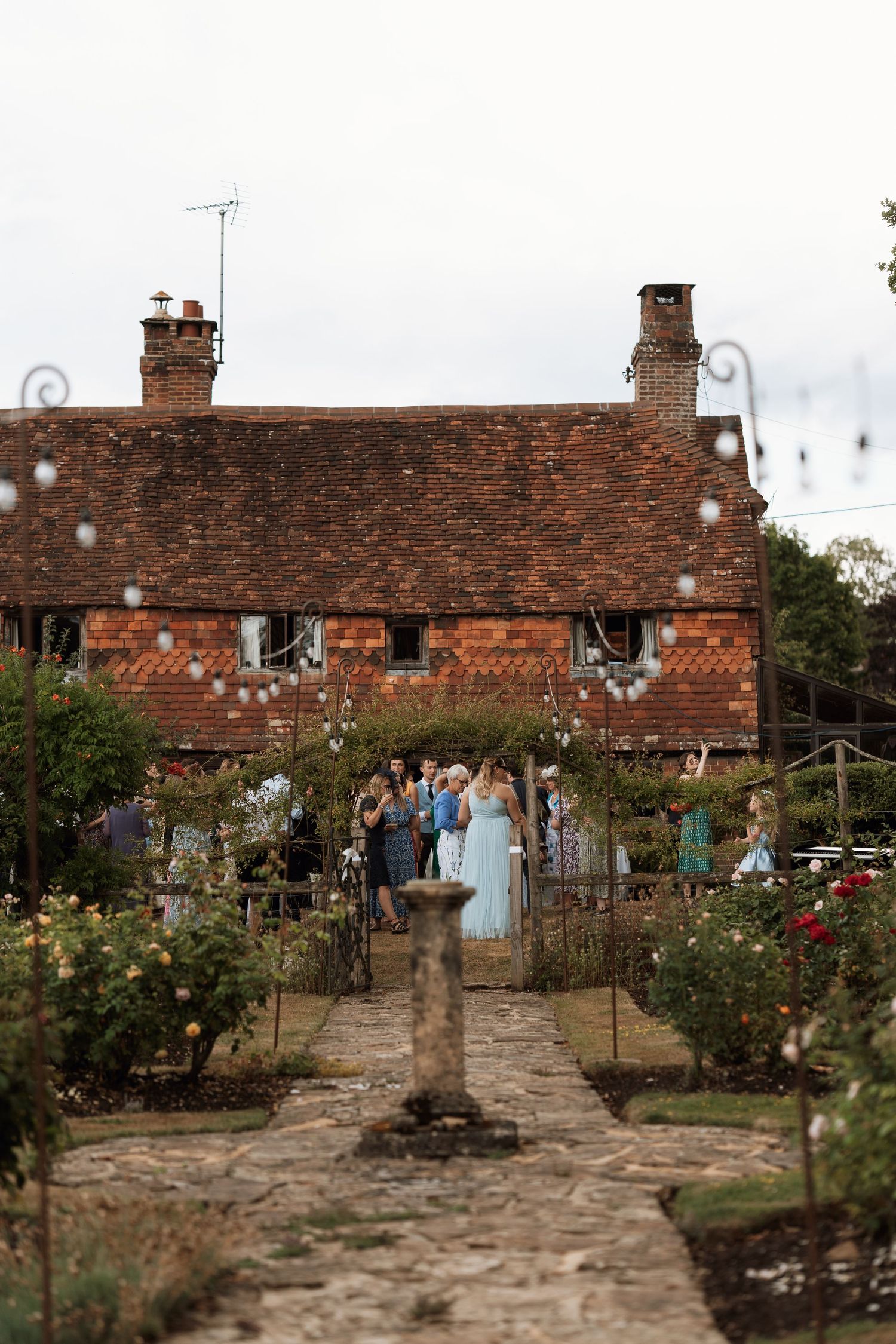 A charming red brick cottage with a garden path leading to a festive outdoor wedding celebration.