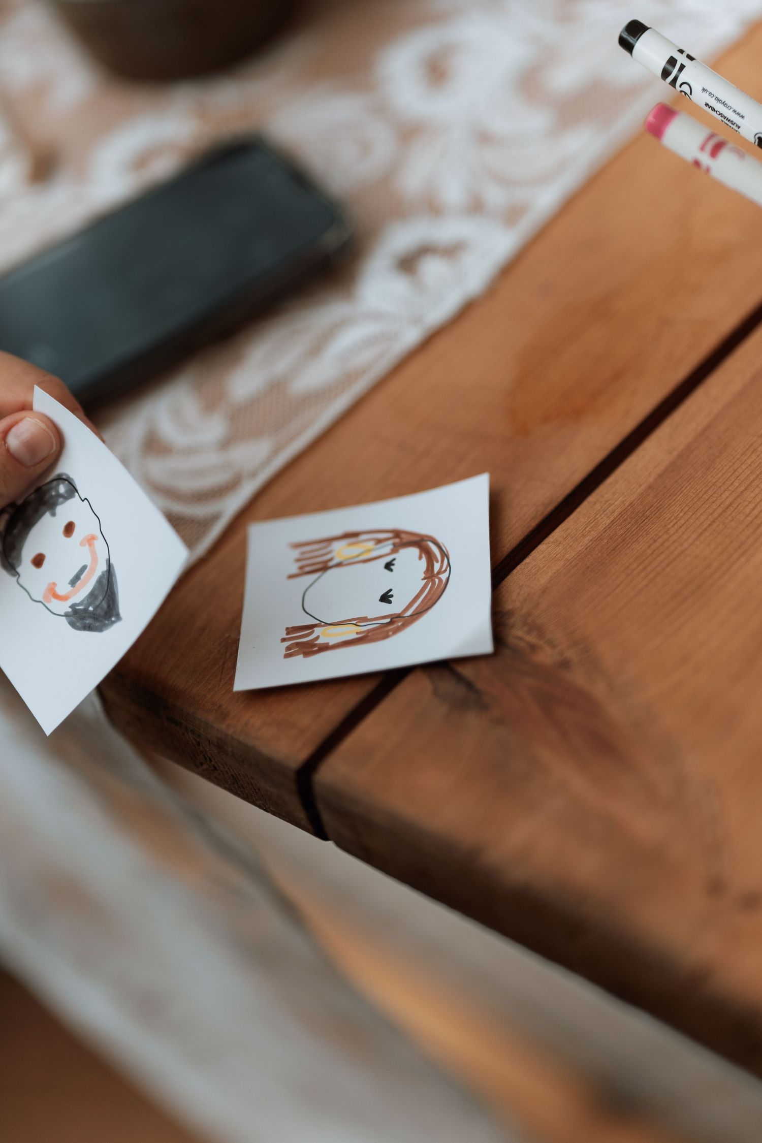 Hand-drawn whimsical sketches displayed on wooden table with white lace accents.